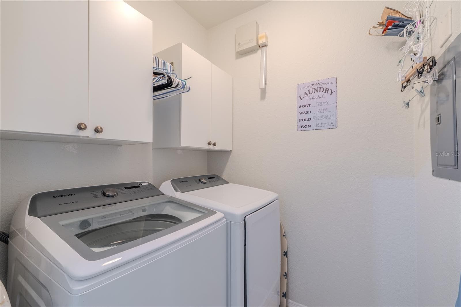 This dedicated interior laundry closet features a full-size washer and dryer, overhead cabinetry for storage, hanging space, and convenient access to the electrical panel, making everyday chores efficient and well organized. - 2738 VIA TIVOLI #220B, CLEARWATER