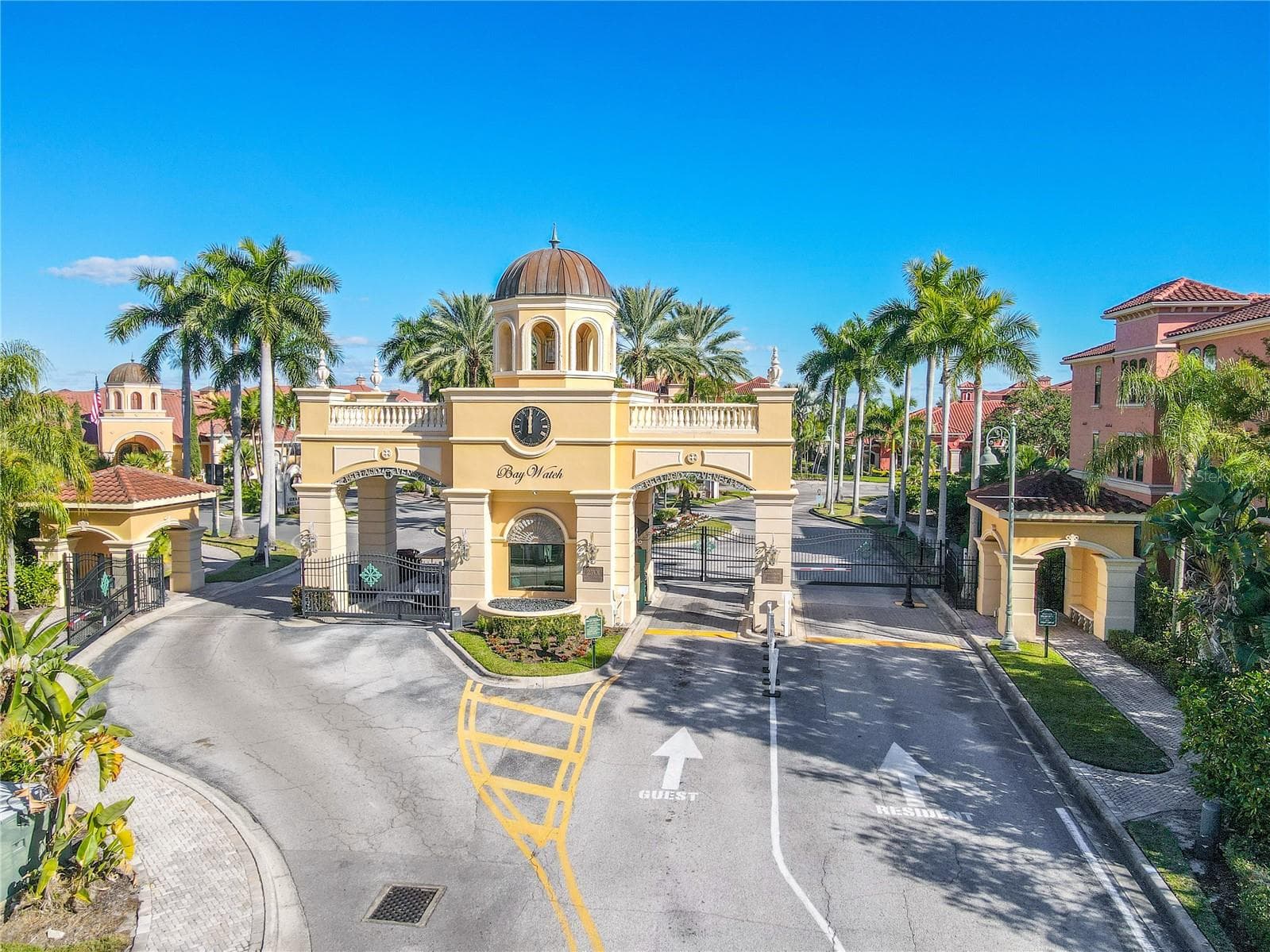 Impressive gated entrance to the Grand Bellagio condo community, featuring a grand clock-tower entry, lush palm-lined landscaping, and a beautifully maintained, resort-style community setting. - 2738 VIA TIVOLI #220B, CLEARWATER