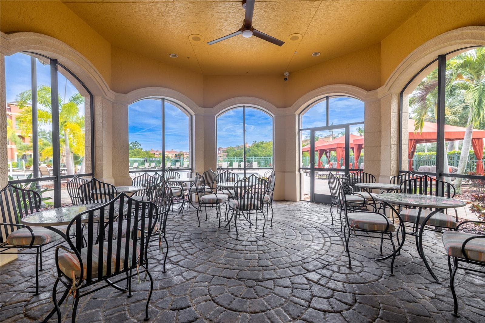 Covered poolside pavilion with café-style seating, ceiling fan, and charming arched openings—perfect for relaxing in the shade while enjoying views of the resort-style pool and cabanas. - 2738 VIA TIVOLI #220B, CLEARWATER