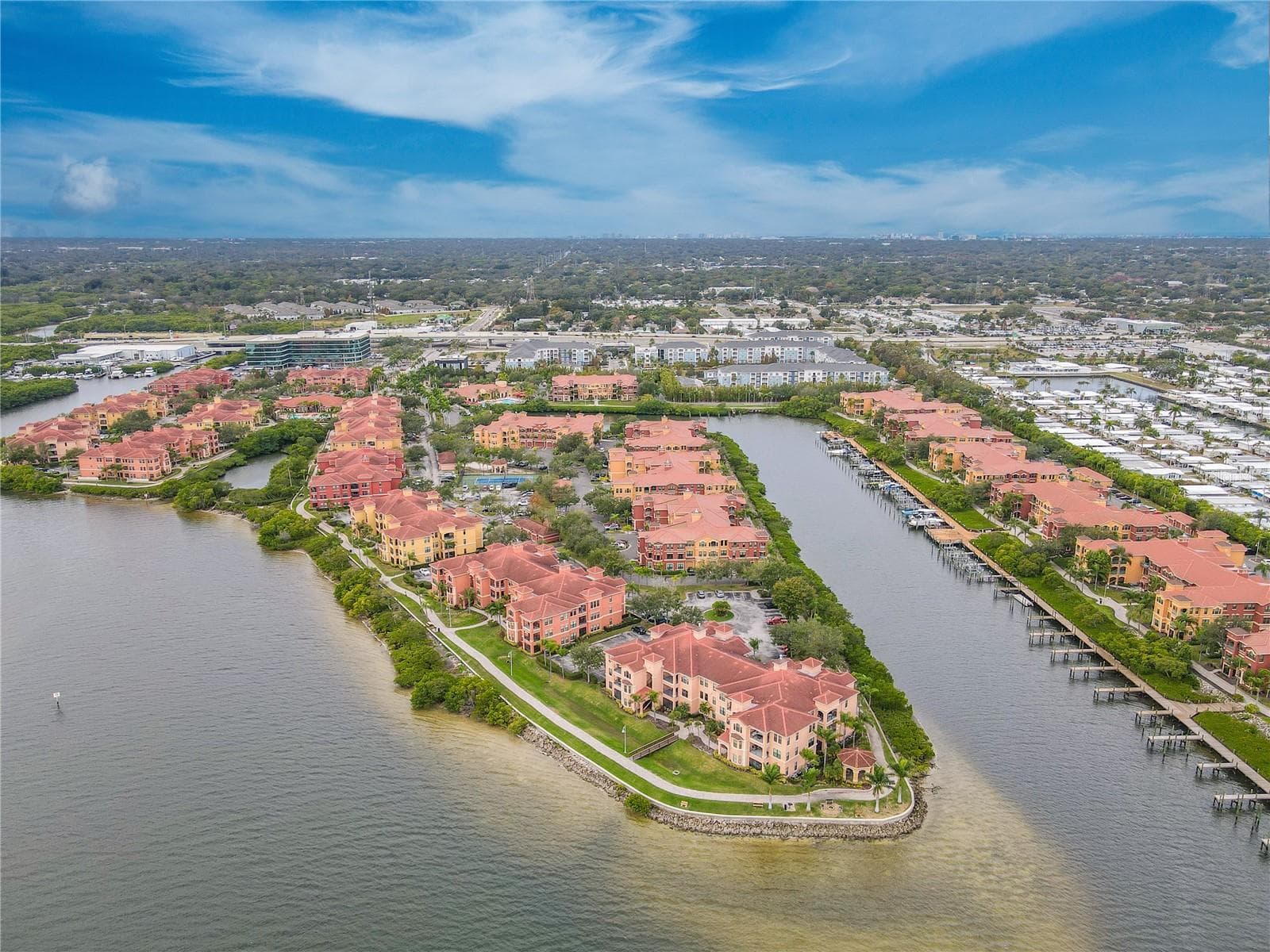 Another elevated aerial waterside view highlights the Mediterranean-style architecture of the Grand Bellagio community, showcasing tile-roofed buildings, palm-lined grounds. - 2738 VIA TIVOLI #220B, CLEARWATER