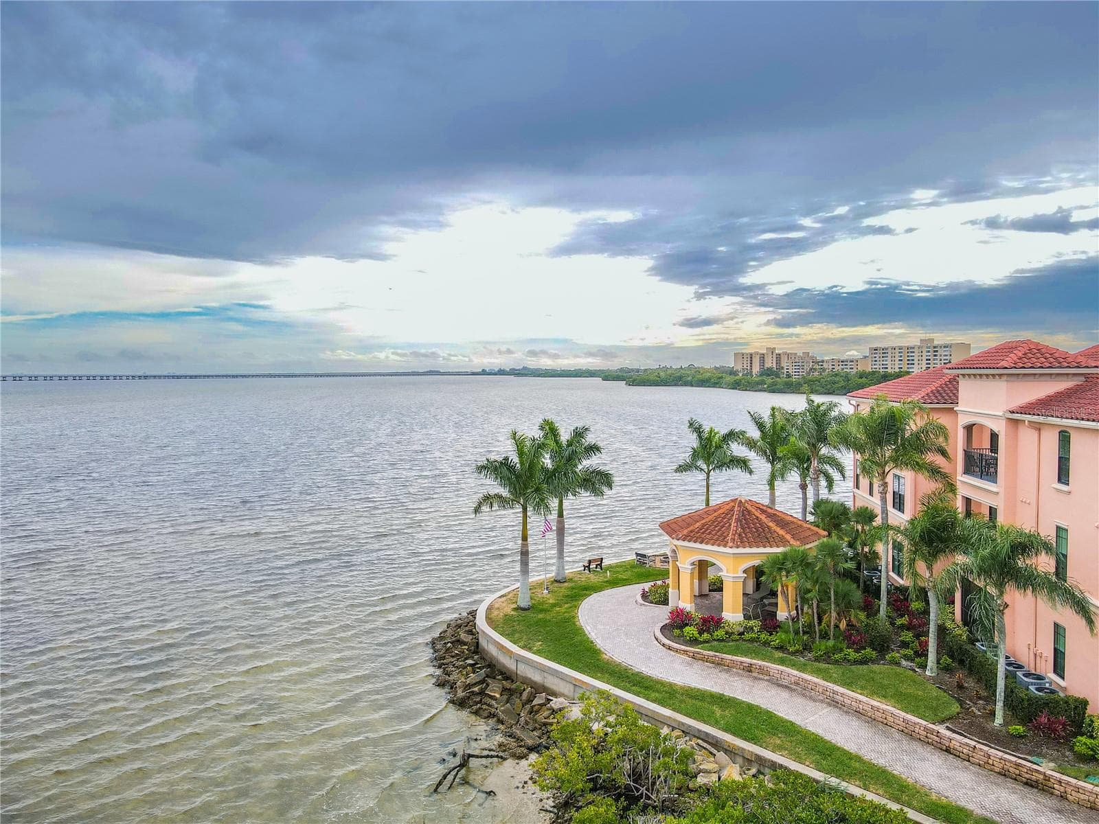 Another elevated aerial waterside view highlights the Mediterranean-style architecture of the Grand Bellagio community, showcasing tile-roofed buildings, palm-lined grounds. - 2738 VIA TIVOLI #220B, CLEARWATER