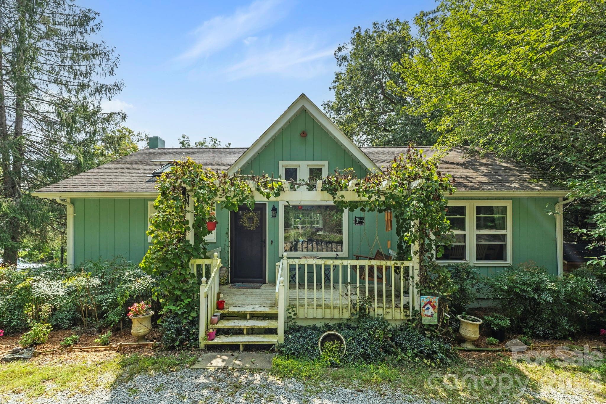 Charming cottage-style home nestled on a scenic corner lot and beautifully landscaped for curb appeal and character. The inviting front porch, framed by a flowering pergola, features classic white railings and is perfect for morning coffee or rocking-chair relaxation. Mature shade trees and thoughtfully designed gardens create a welcoming entry, while the home's classic architectural character blends seamlessly with modern updates. Conveniently located on a scenic corner lot, walkable to Brevard Elementary and High Schools, Silvermont Park, and downtown Brevard. - Brevard