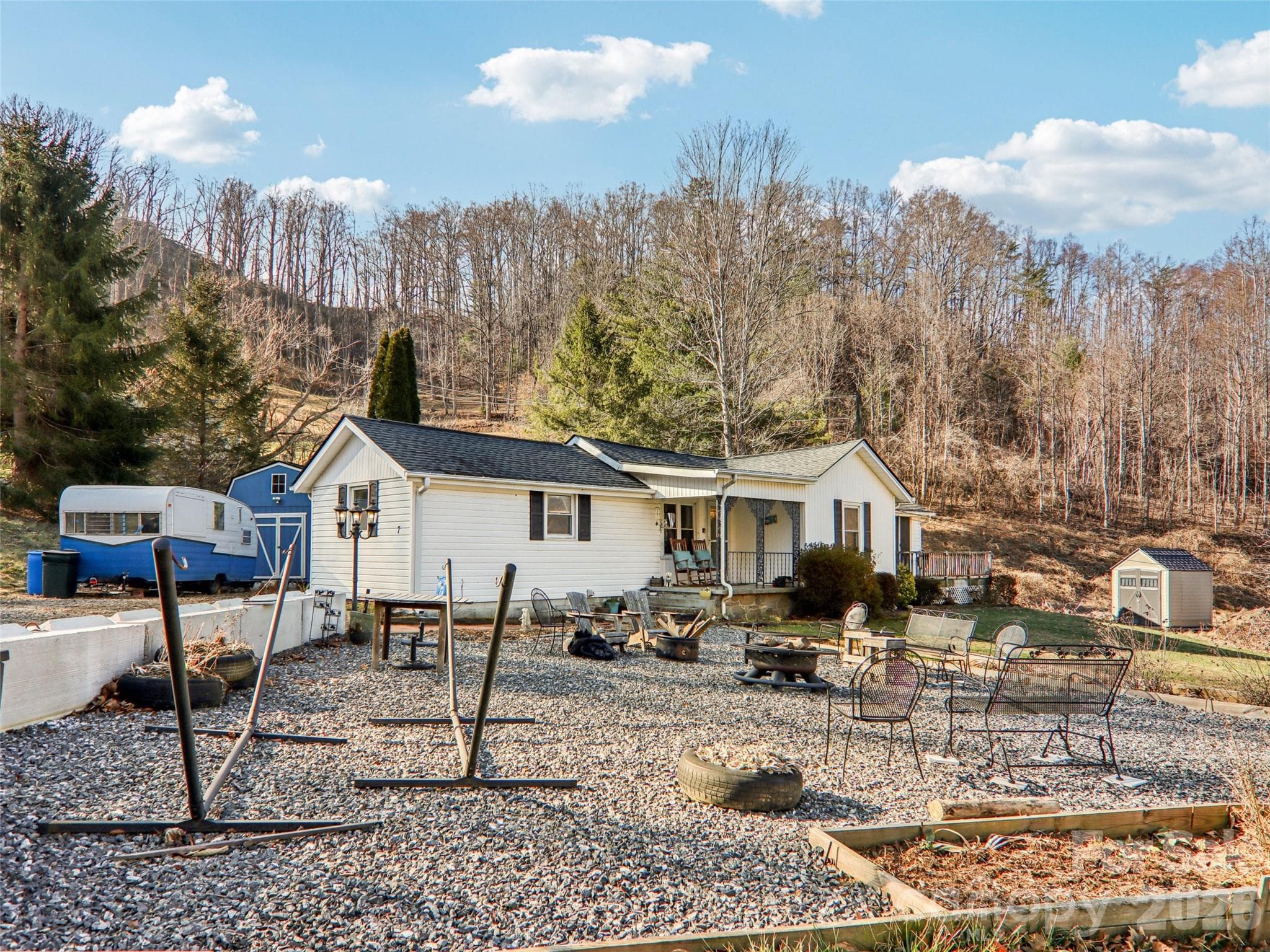 Gravel patio and outdoor seating area located in the front yard, offering a flexible space for relaxing or entertaining with views of the surrounding natural landscape and wooded hillside backdrop - Weaverville