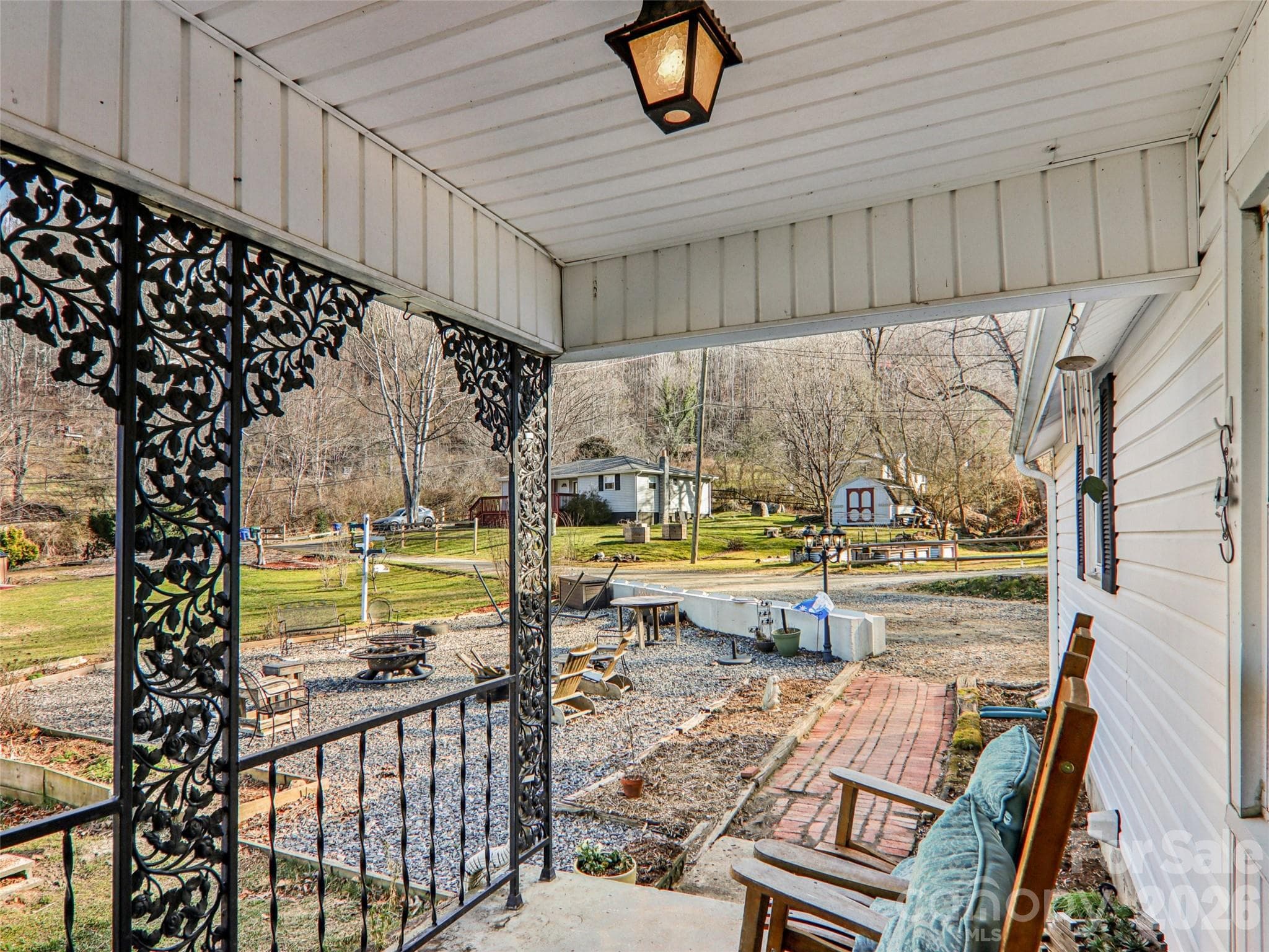 Covered front porch with decorative ironwork, offering a comfortable spot to relax while overlooking the front yard, gravel patio, and outdoor gathering area. - 7 Landon Mountain Lane, Weaverville