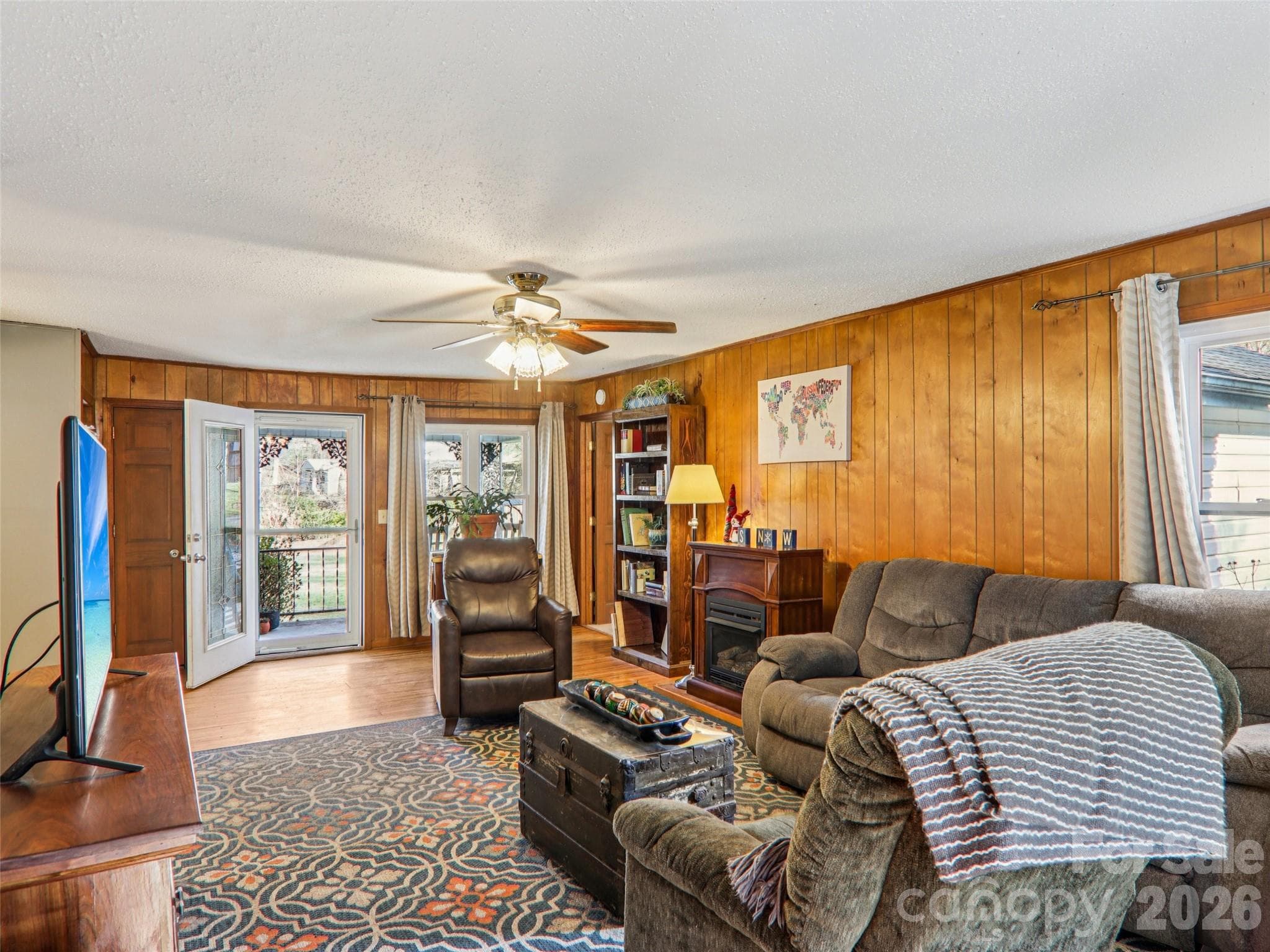 Living room view oriented toward the front door, highlighting wood-paneled walls, ceiling fan, natural light, and access to the covered front porch. - 7 Landon Mountain Lane, Weaverville