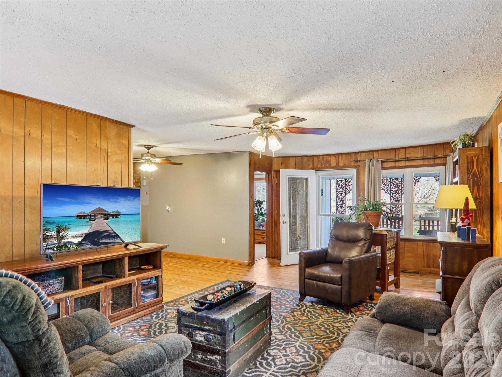 Living room view looking toward the front entry and dining area, highlighting the open layout, wood-paneled walls, ceiling fan, and natural light throughout the space - 7 Landon Mountain Lane, Weaverville