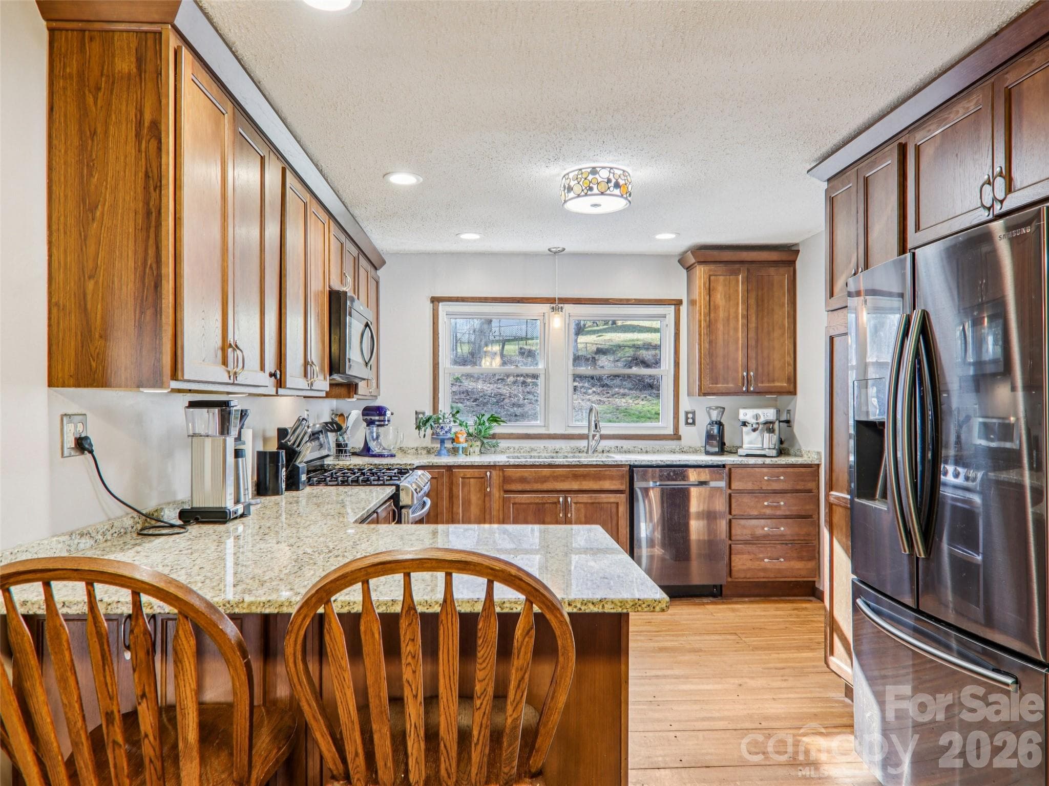 Updated kitchen viewed from the dining area, featuring granite countertops, wood cabinetry, stainless steel appliances, and generous counter space, with natural light from the window over the sink and direct access to the wrap-around deck. - 7 Landon Mountain Lane, Weaverville