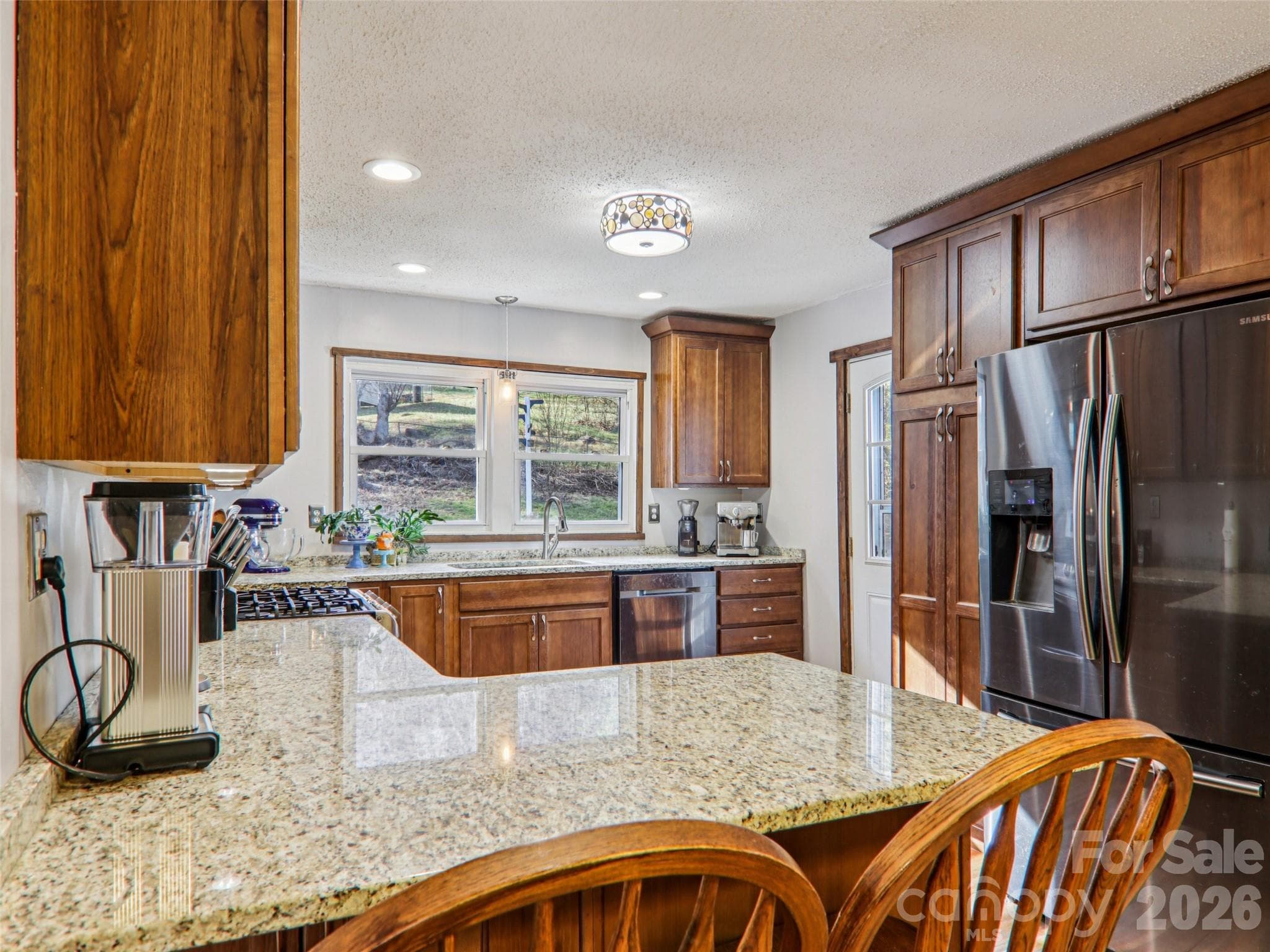 Alternate view of the updated kitchen showcasing granite countertops, wood cabinetry, stainless steel appliances, ample counter space, and back door access to the wrap-around deck. - 7 Landon Mountain Lane, Weaverville