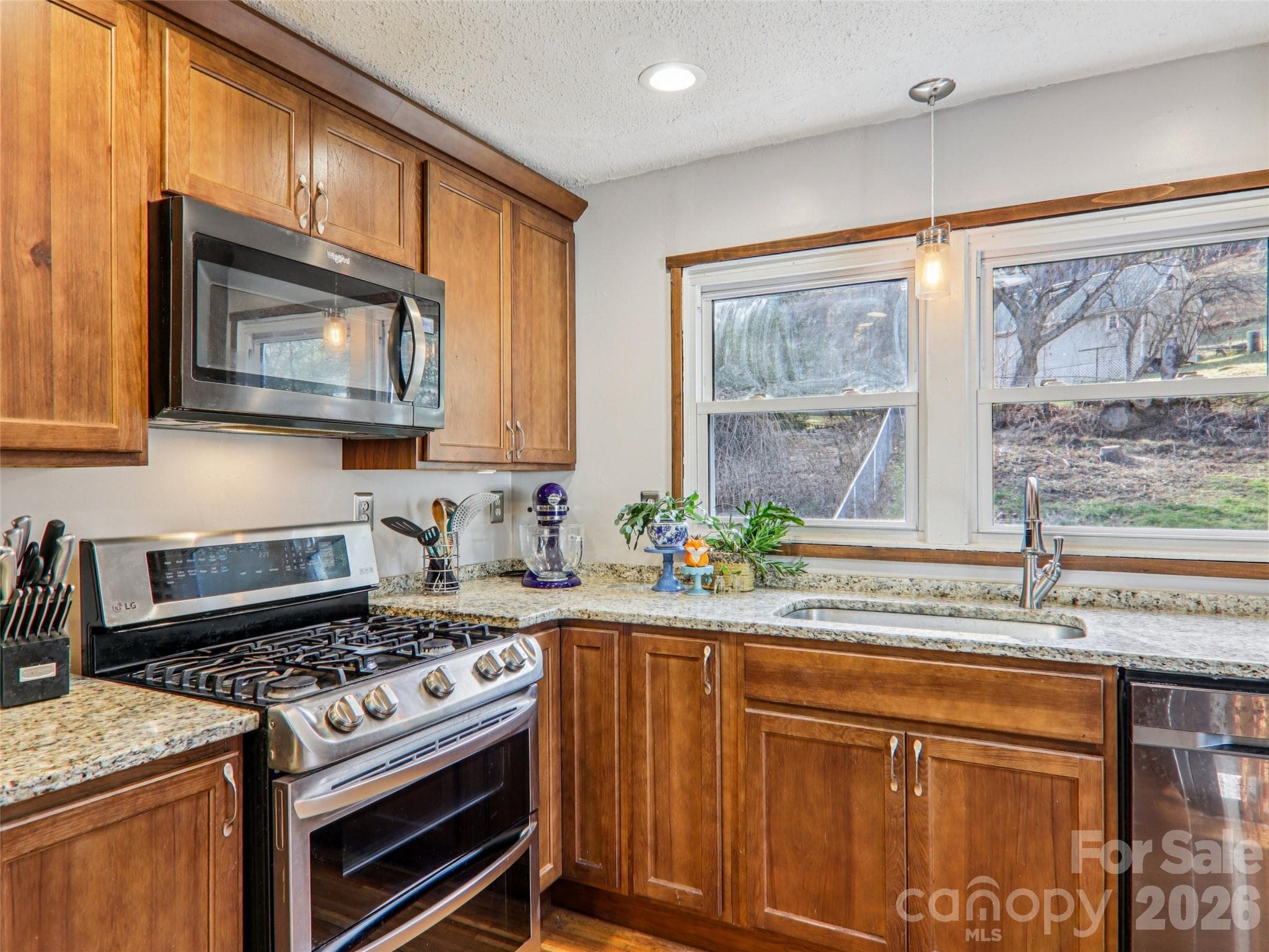 Closer view of the updated kitchen highlighting granite countertops, wood cabinetry, stainless steel range and microwave, window over the sink, and clean, functional workspace. - 7 Landon Mountain Lane, Weaverville