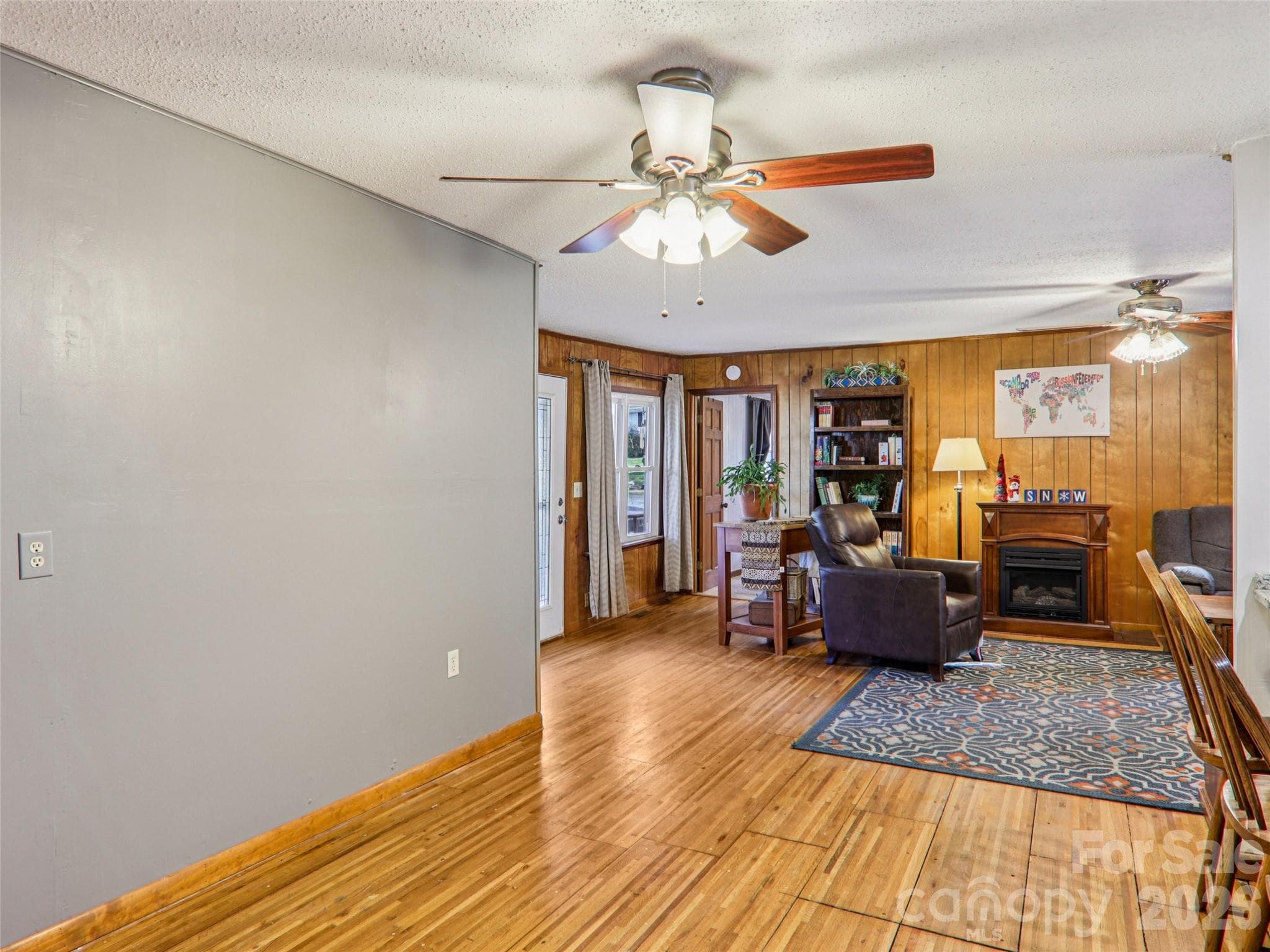 Dining area with hardwood floors, opening into the living room with wood-paneled walls and a gas fireplace - 7 Landon Mountain Lane, Weaverville