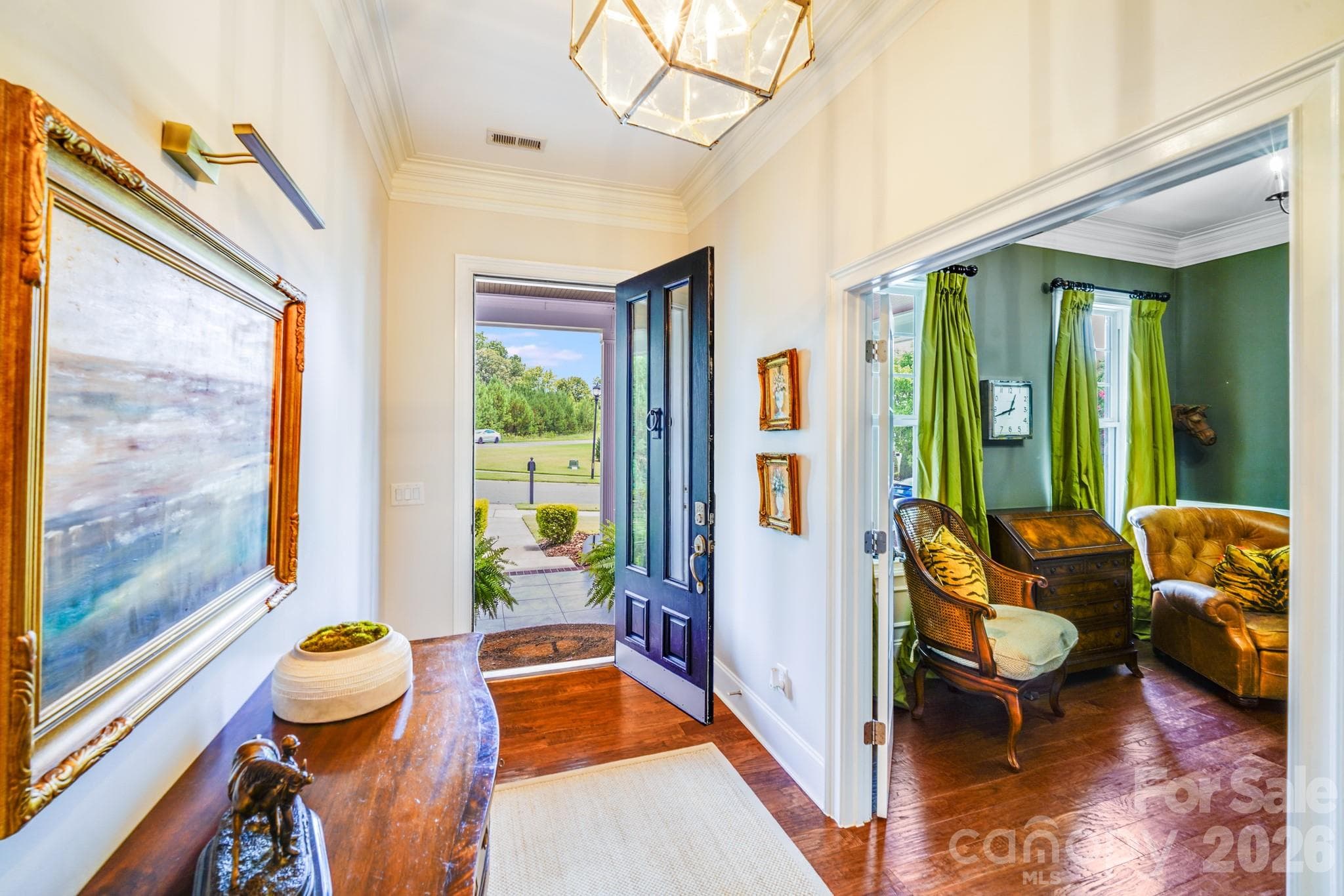 A striking black front door features vertical glass panels that flood the foyer with natural light, warm hardwood floors contrast beautifully with the crisp white trim and neutral walls - 2702 Arsdale Road, Waxhaw