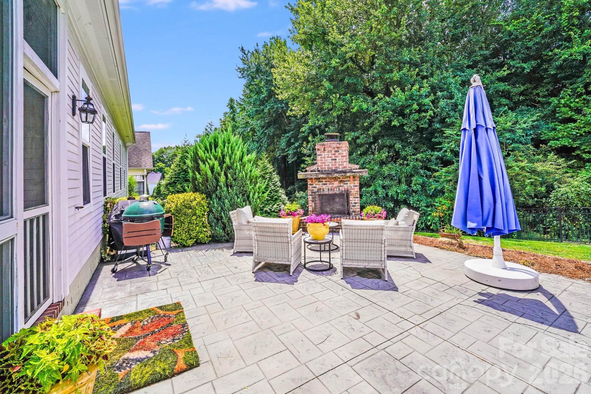 Expansive stamped concrete patio offers a seamless flow from indoor to outdoor living, complete with a built-in brick fireplace, vibrant landscaping, and ample space for grilling, relaxing, or entertaining - 2702 Arsdale Road, Waxhaw