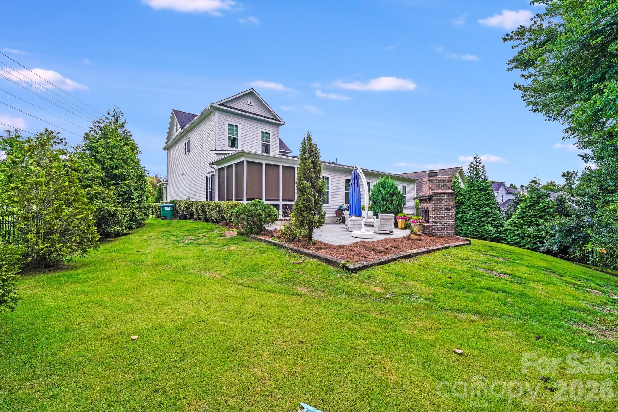 This wide view showcases the expansive backyard and the beautifully elevated stamped-concrete patio, where a cozy brick fireplace and lush landscaping create a peaceful, private outdoor retreat - 2702 Arsdale Road, Waxhaw