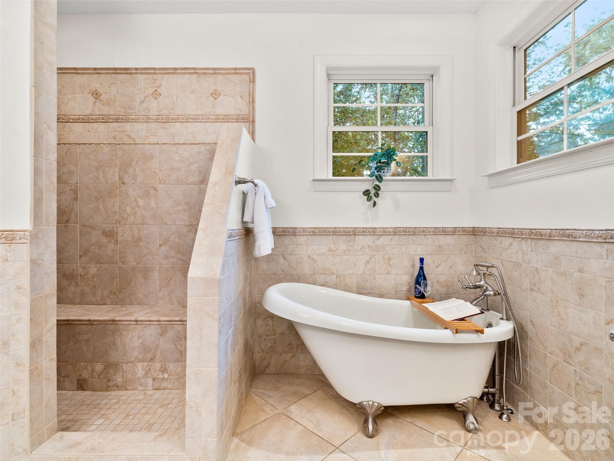 This master bathroom features a relaxing soaking tub, a spacious open tiled shower, and windows that fill the space with natural light, creating a serene, spa-like retreat. - Asheville