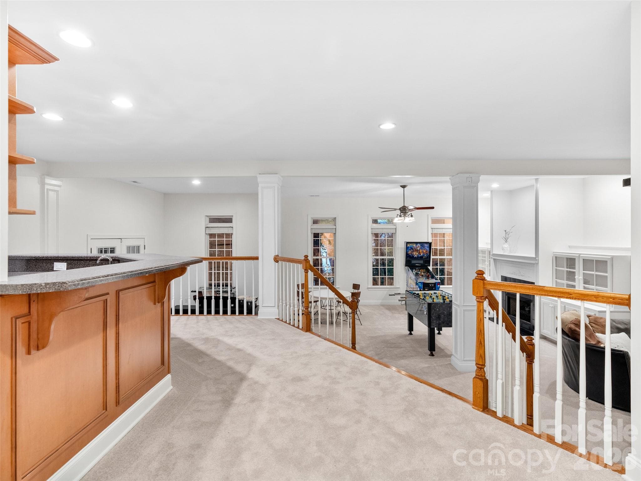 This secondary kitchen area overlooks the rec room, featuring attractive wooden spindle railings and a clear view of the cozy gas fireplace, creating a warm and connected gathering space. - Asheville