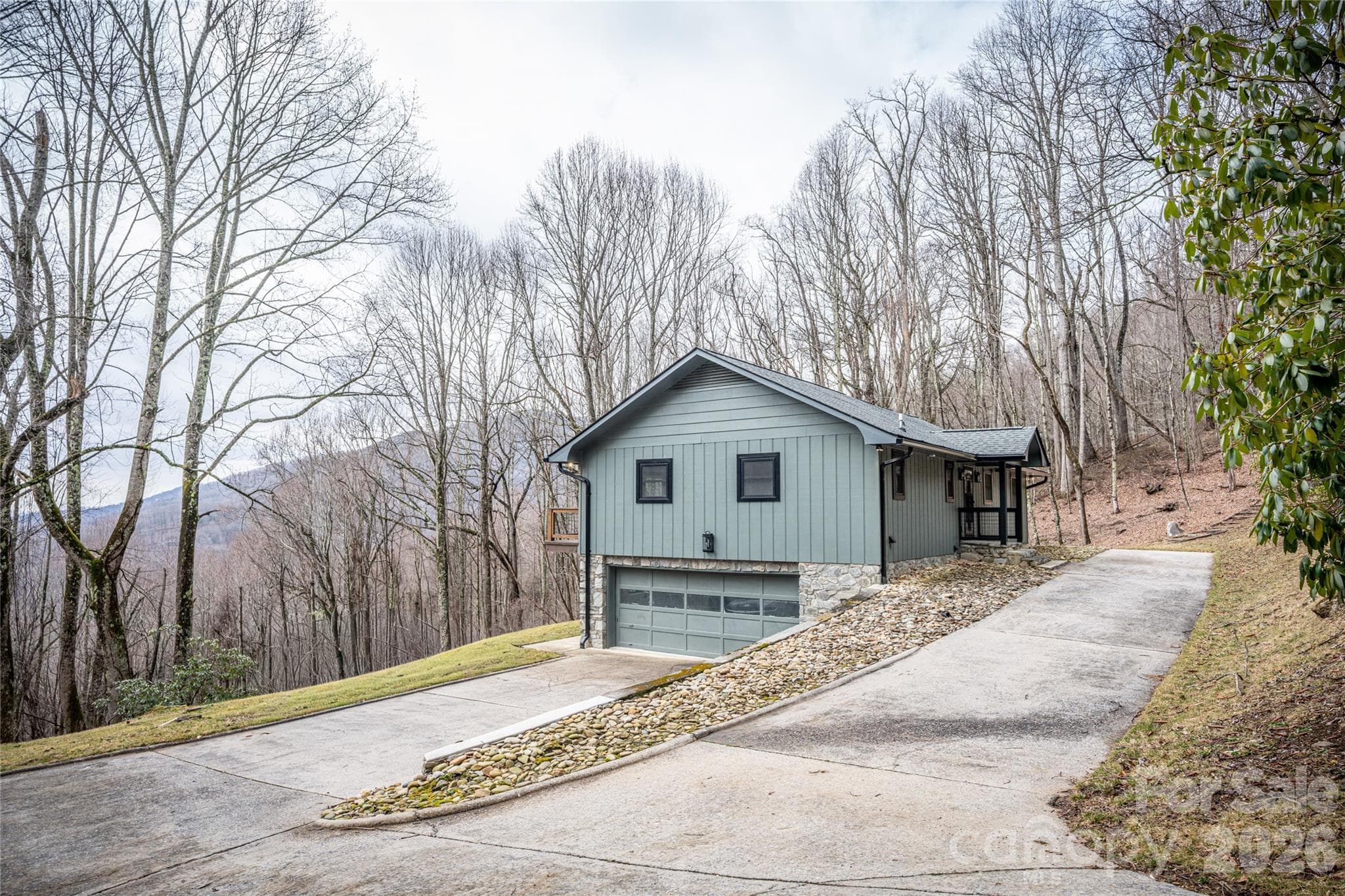Long concrete driveway provides ample parking and easy access to the two-car garage. Stone foundation details and updated exterior finishes highlight the home’s complete renovation. - Waynesville