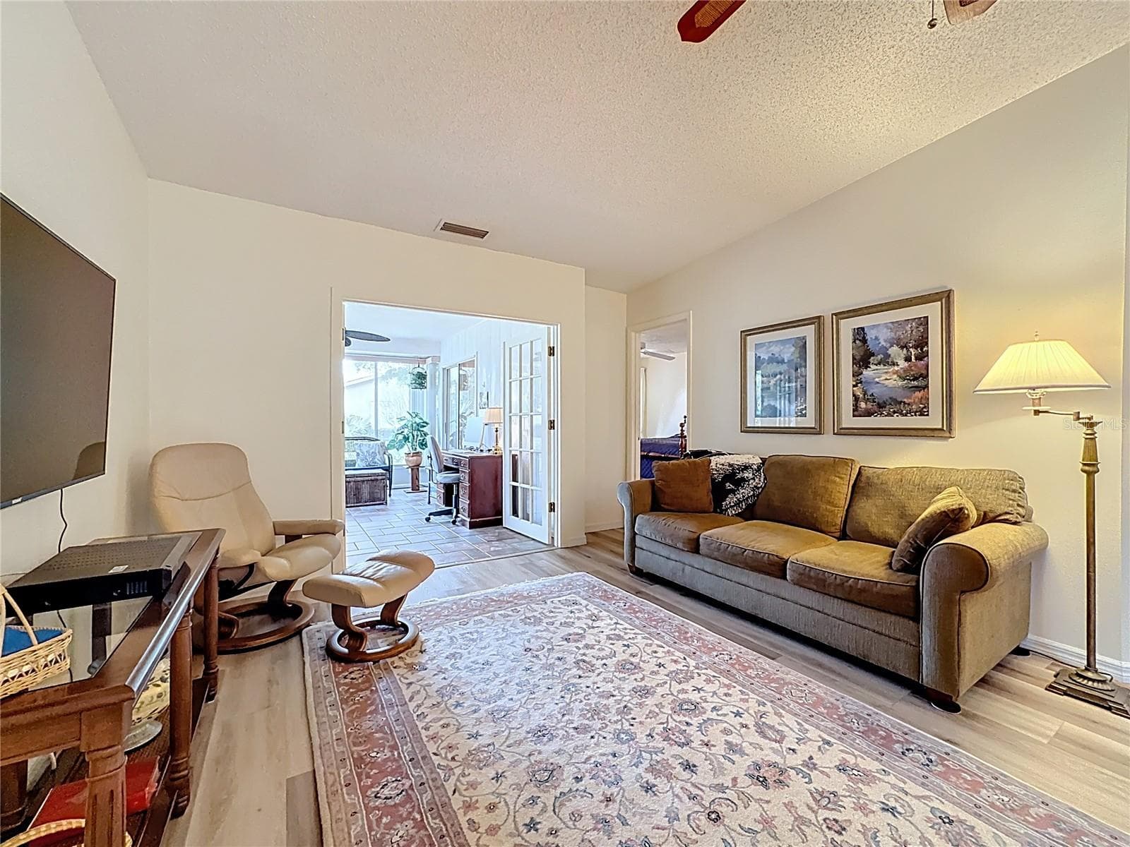 Another view of the family room with French doors leading into air conditioned Florida room and primary suite to the left of the couch. - 5611 GARDEN LAKES DR, BRADENTON