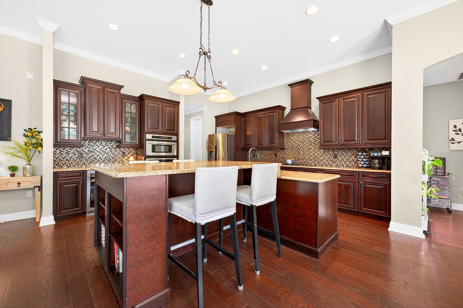 At the center of it all is the gorgeous chef’s kitchen, designed to impress with an OVERSIZED ISLAND offering seating on both sides, granite countertops, rich cabinetry, decorative backsplash, STAINLESS STEEL APPLIANCES, beverage refrigerator, and the brand new cooktop with a custom range hood that seamlessly matches the cabinetry. - 27324 GRAND OAK LN, TAVARES