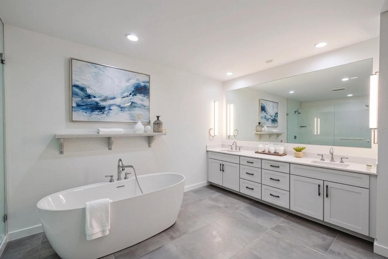 The primary bathroom features a sophisticated double vanity with an expansive quartz countertop, dual undermount sinks, and abundant drawer storage. Sleek brushed nickel hardware and soft-close cabinetry complement the clean, modern aesthetic. A full-width mirror framed by contemporary vertical sconces provides excellent lighting and adds to the spa-like ambiance of this beautifully designed space. - 920 N OSCEOLA AVE #703, CLEARWATER