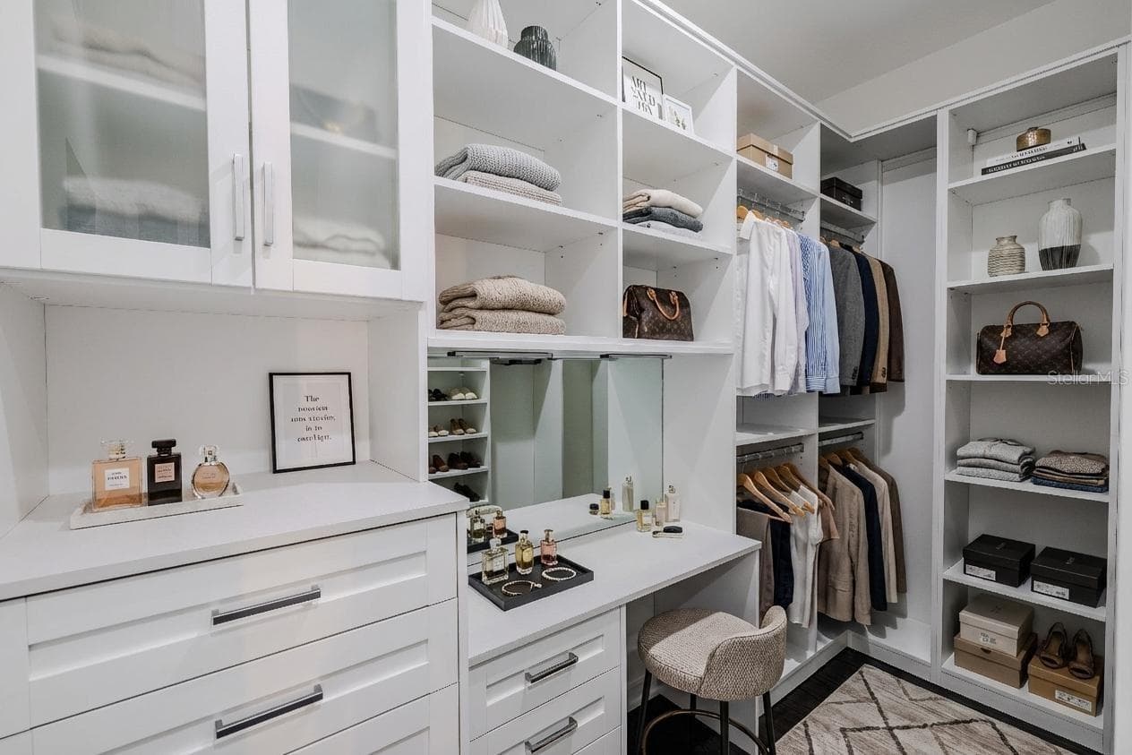 The secondary primary closet offers exceptional organization and functionality, featuring custom built-ins with open shelving, drawers, and hanging space. Frosted glass cabinet doors add a touch of elegance, while a built-in vanity with mirror and ample countertop space provides a perfect spot for getting ready. Thoughtfully designed to maximize storage and style - 920 N OSCEOLA AVE #703, CLEARWATER