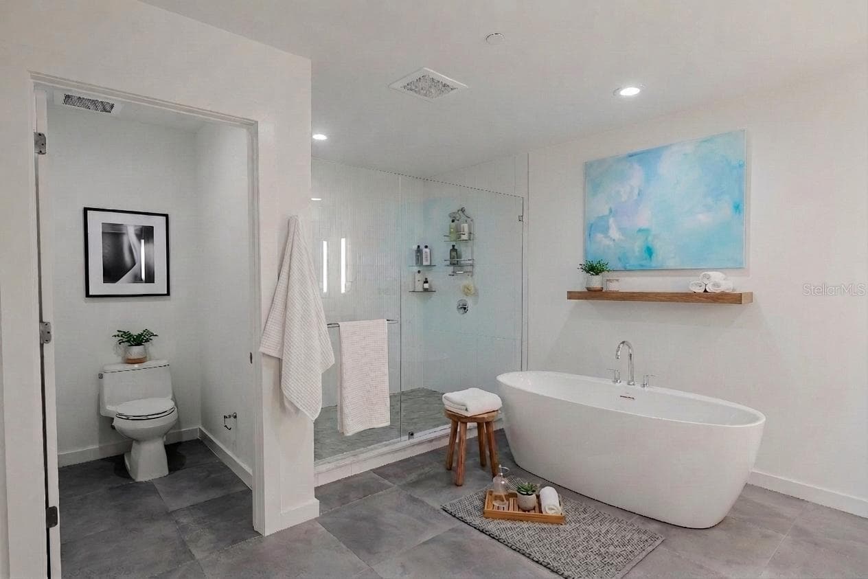 The luxurious primary bathroom exudes spa-like serenity with a sleek, modern design. A private water closet, a freestanding soaking tub serves as the elegant focal point, complemented by a frameless glass-enclosed walk-in shower - 920 N OSCEOLA AVE #703, CLEARWATER