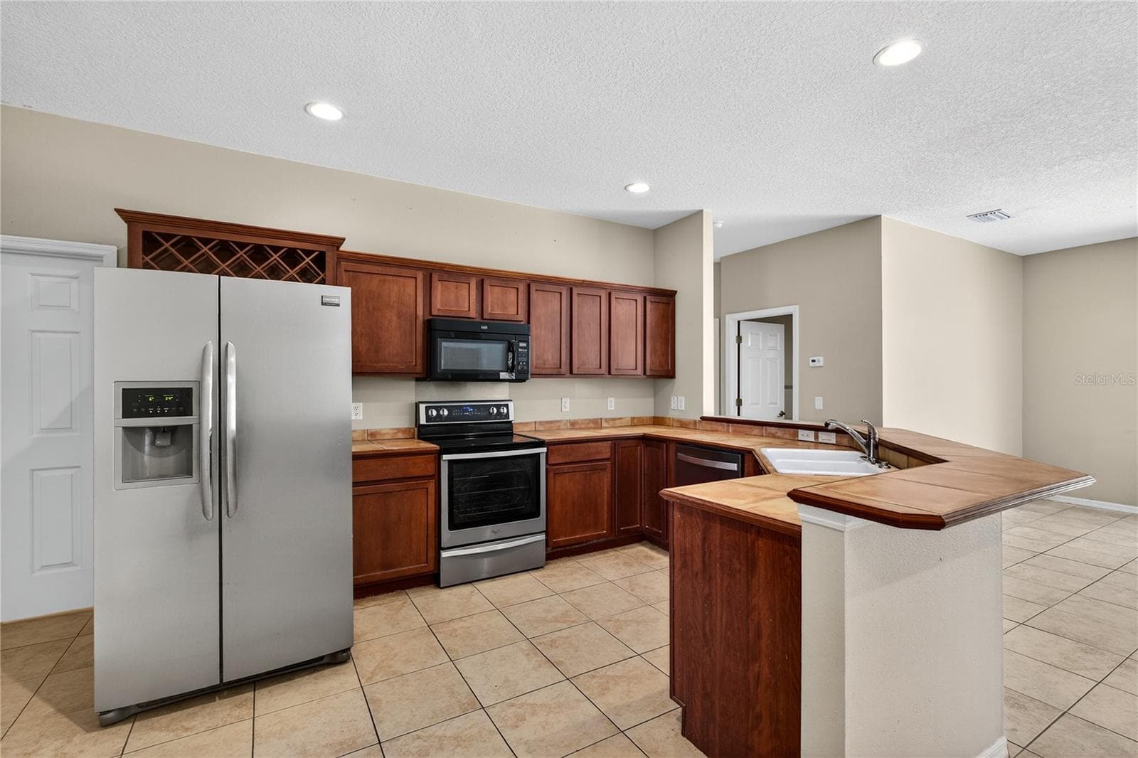 Spacious kitchen boasts tile counters, wood cabinets, offering a warm and inviting space for culinary creations and everyday gatherings. - 28931 BEAUCLAIRE DR, TAVARES