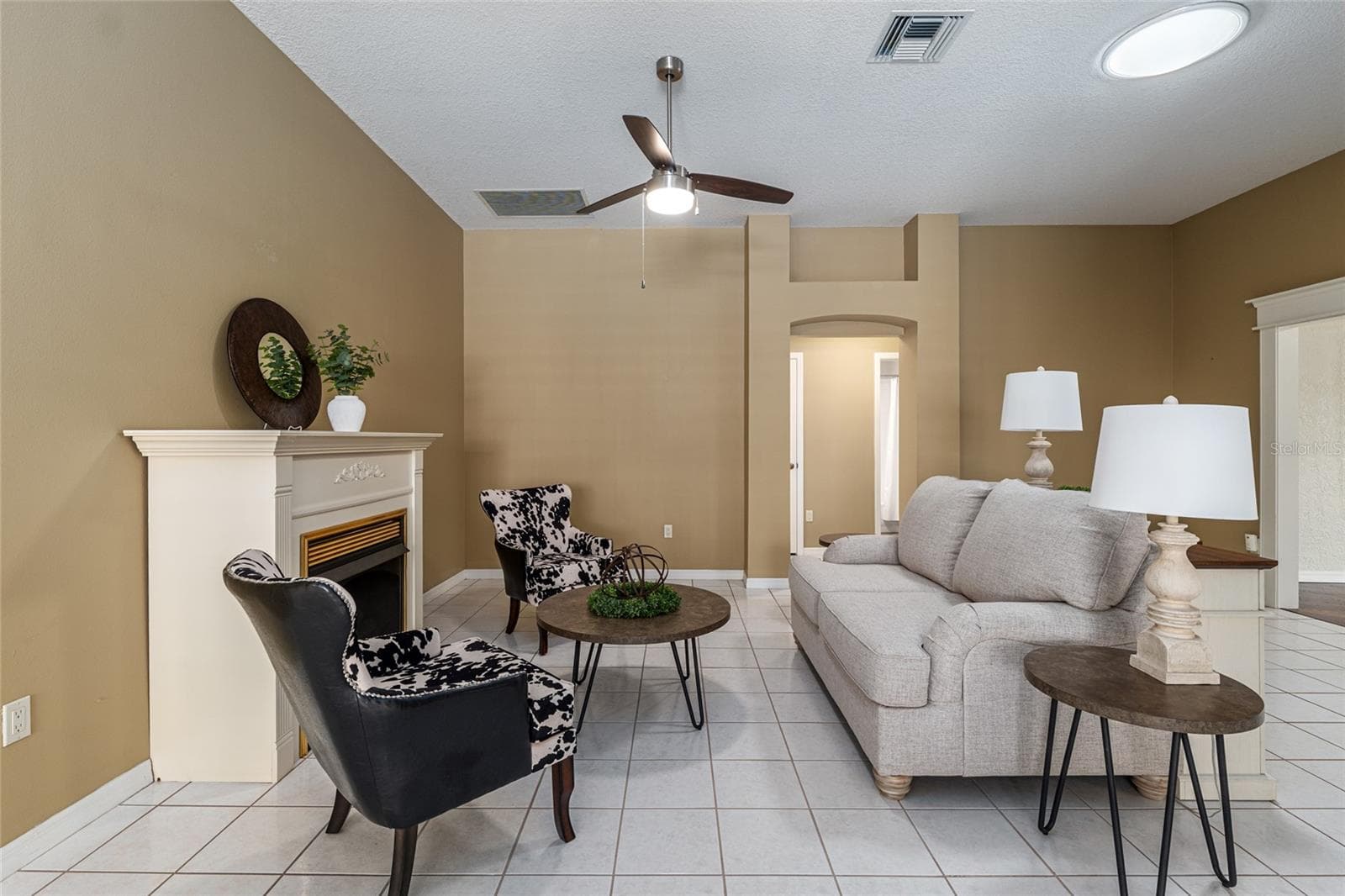 Living Room: Comfortable living area with tile flooring, ceiling fan, and a fireplace that serves as a cozy focal point. - 110 CHULA VISTA AVE, LADY LAKE