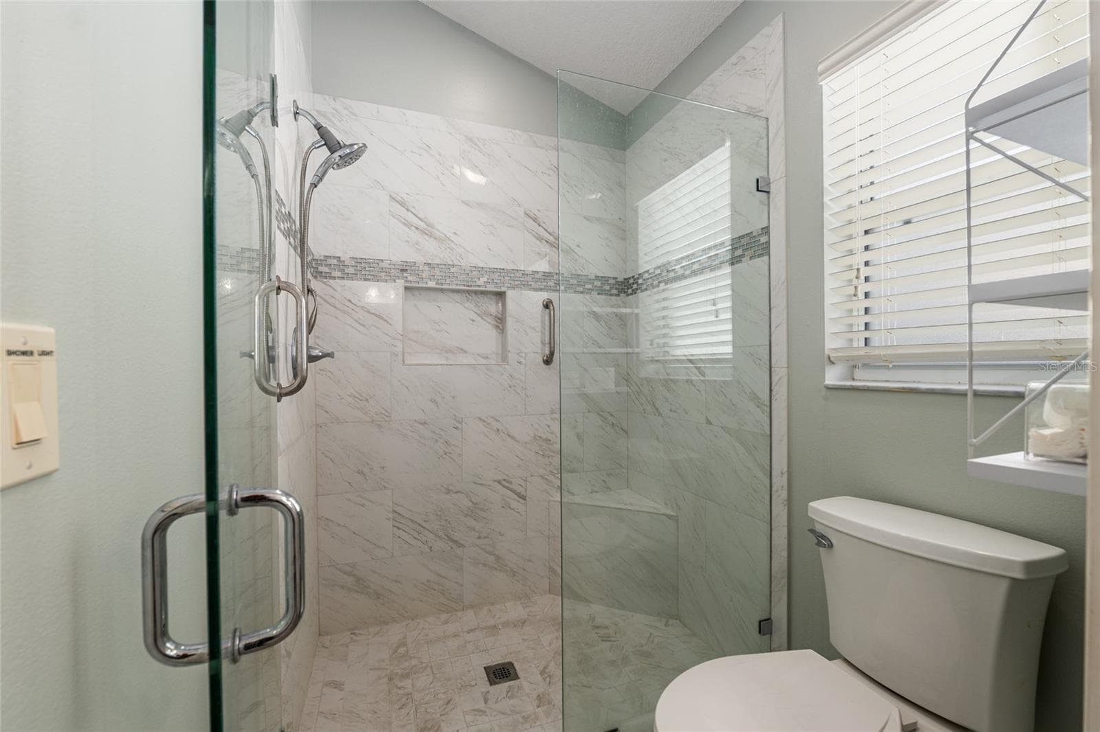 Primary Shower: Walk-in shower with tile surround, glass enclosure, and built-in niche offers a clean, modern design. - 110 CHULA VISTA AVE, LADY LAKE