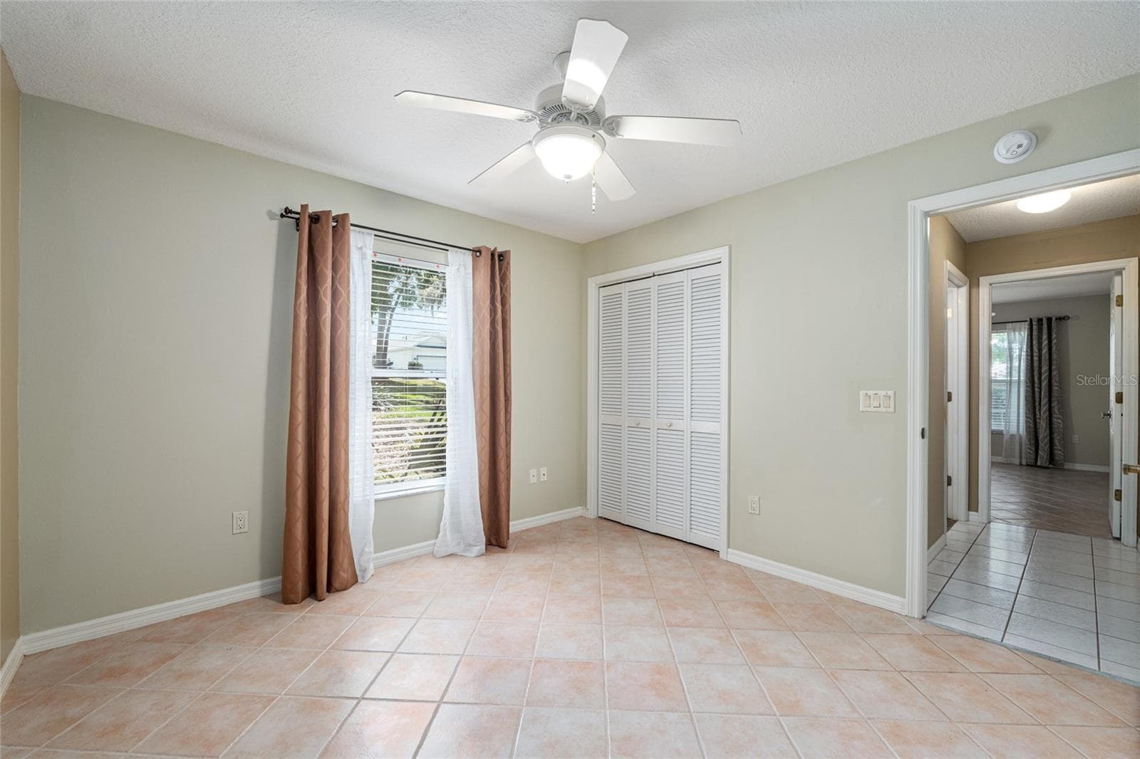 Secondary Bedroom: Secondary bedroom features tile flooring, a ceiling fan, and a window that brings in natural light. - 110 CHULA VISTA AVE, LADY LAKE