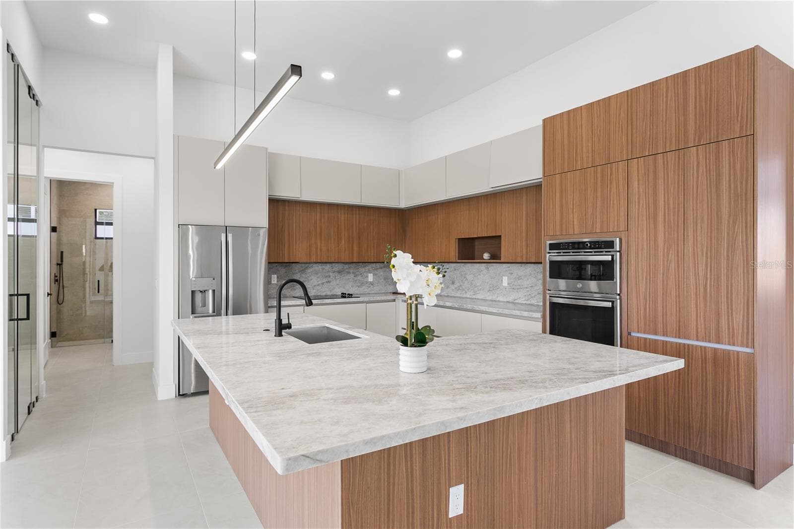 The CHEF'S KITCHEN offers OVERSIZED L-SHAPED ISLAND w/ MARBLE COUNTERTOP & extra entertainment space! Custom cabinetry, MARBLE TAJ MAHAL COUNTERTOPS w/ FULL BACKSPLASH, large pantry & premium GE appliances including wall oven, microwave, electric cooktop, dishwasher, refrigerator and freezer, plus a large sink with black fixtures. - 3300 NW 1ST TER, CAPE CORAL