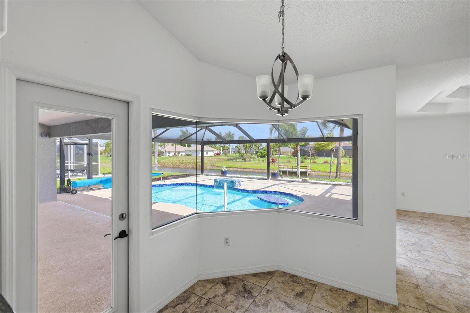 Elegant dining area with chandelier, large windows, and views of the pool - 605 ROTONDA CIR, ROTONDA WEST