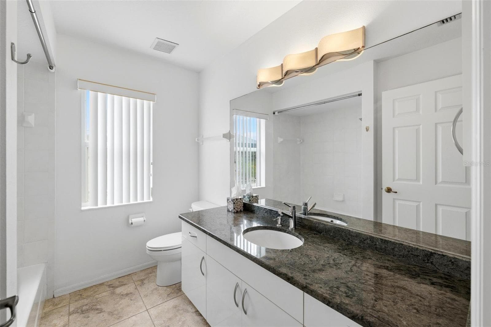 Clean, modern bathroom with dark granite vanity and updated light fixtures - 605 ROTONDA CIR, ROTONDA WEST