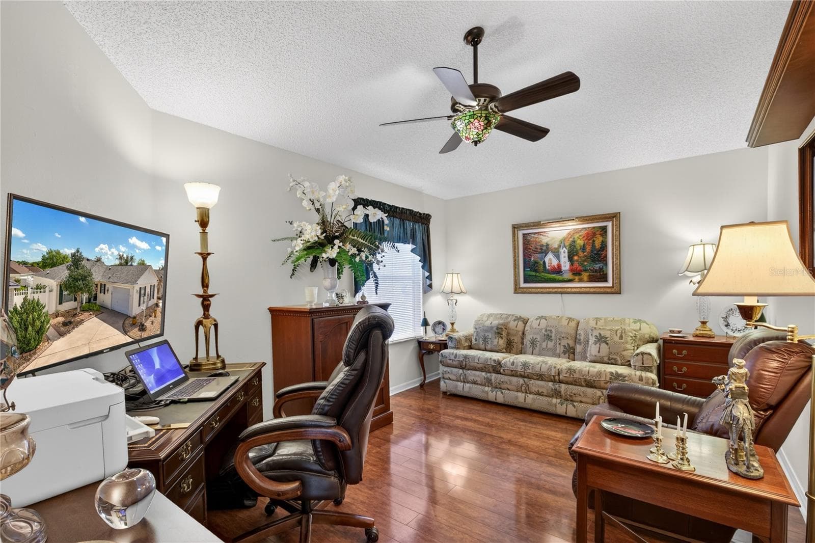 This expansive second bedroom offers a comfortable and inviting space, highlighted by gleaming laminate wood floors. The room is further enhanced by a stylish ceiling fan, complete with a beautiful Tiffany glass light shade. An electric fireplace adds a touch of cozy elegance,. - 1147 ELIZABETH CT, THE VILLAGES