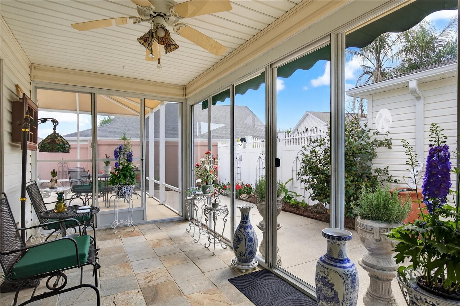 This beautiful property features a  glass-enclosed lanai, complete with  stylish slate tile floors, offering a serene space to relax and enjoy the outdoors. The lanai provides picturesque views of the inviting courtyard, which is beautifully enhanced by lush, vibrant tropical Florida landscaping. - 1147 ELIZABETH CT, THE VILLAGES