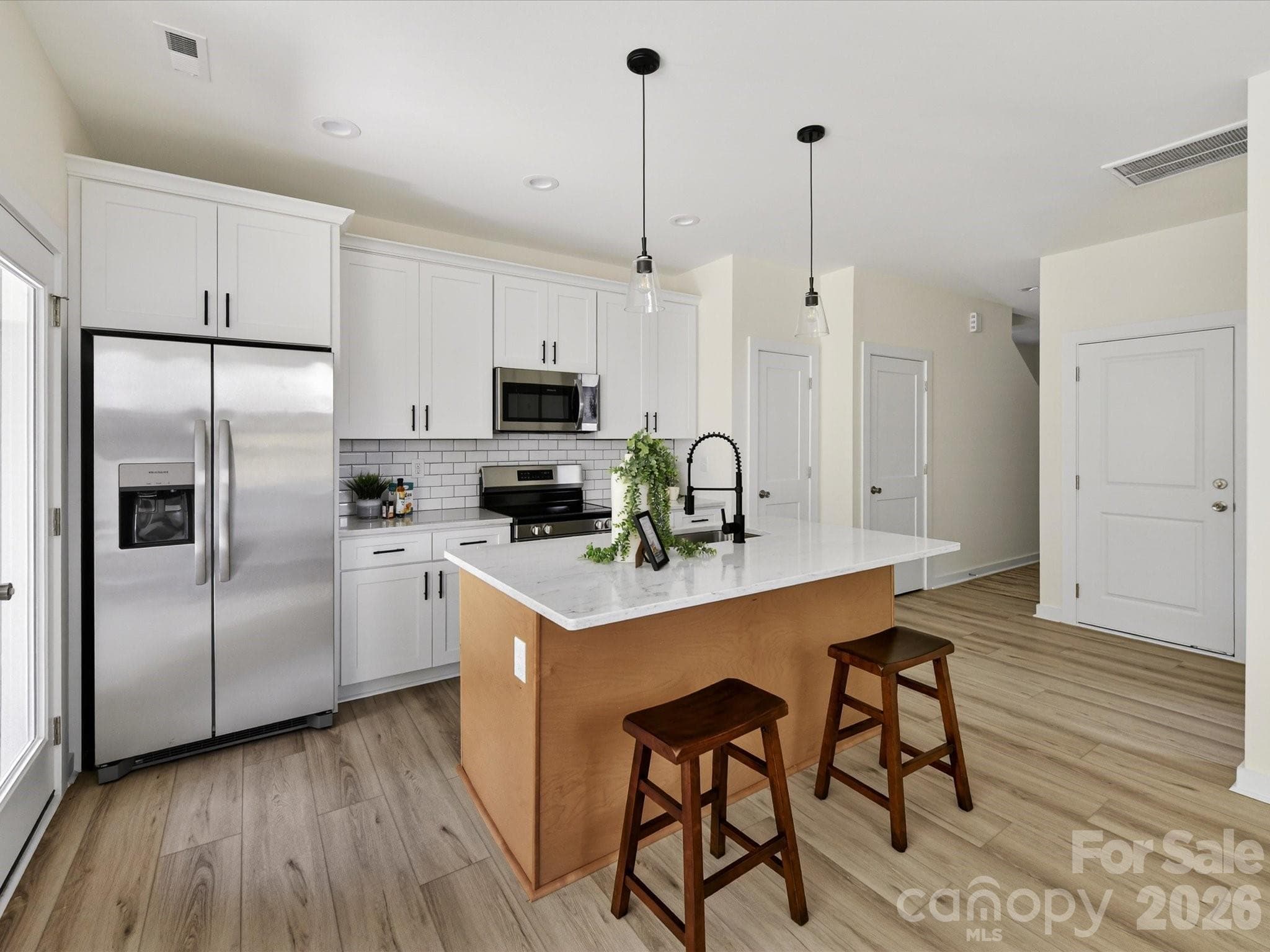 Bright, open-concept kitchen featuring a spacious island with seating, stainless steel appliances, and seamless flow into the sun-filled living area. - Charlotte