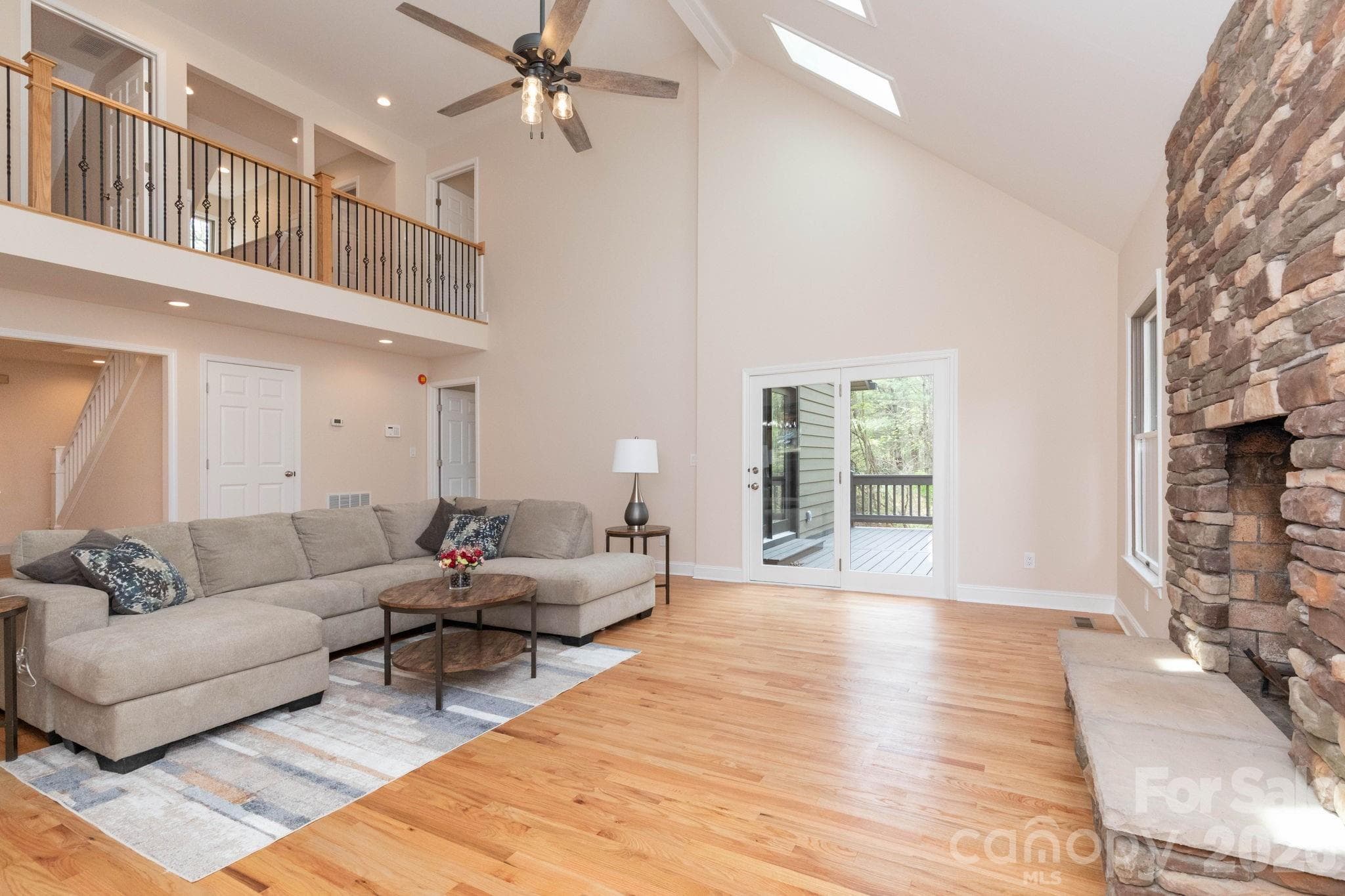Spacious living room with soaring vaulted ceilings, skylights, and a stunning floor-to-ceiling stone fireplace. - Fletcher