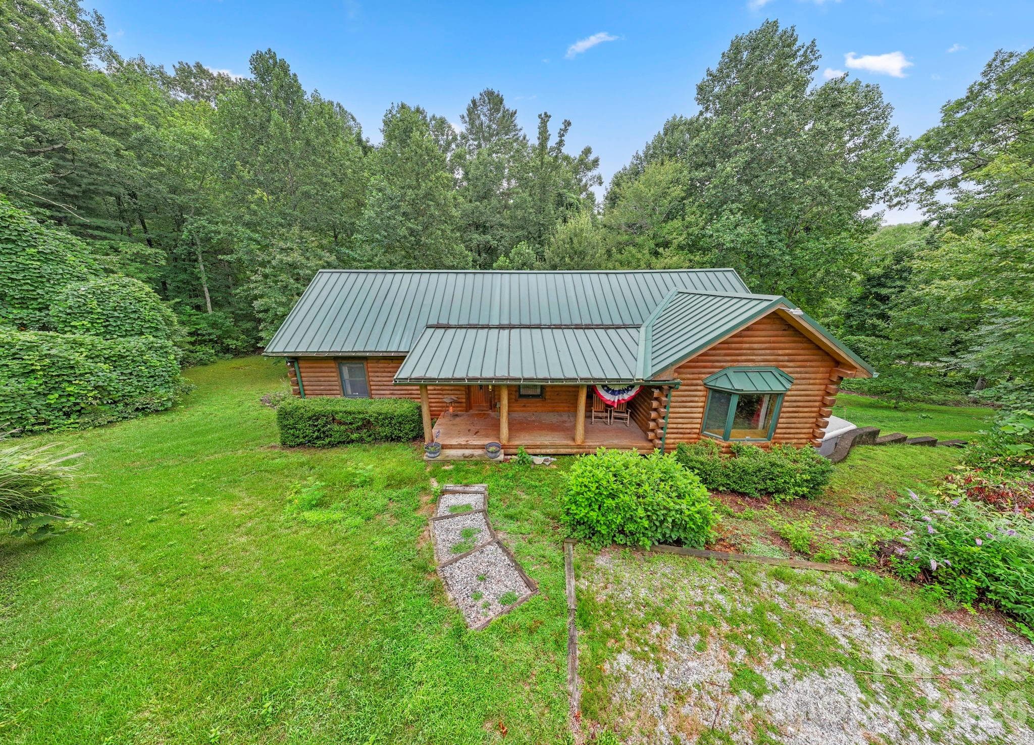 Charming front exterior with covered porch, nestled in a lush, serene landscape. - 266 Rhododendron Drive, Saluda