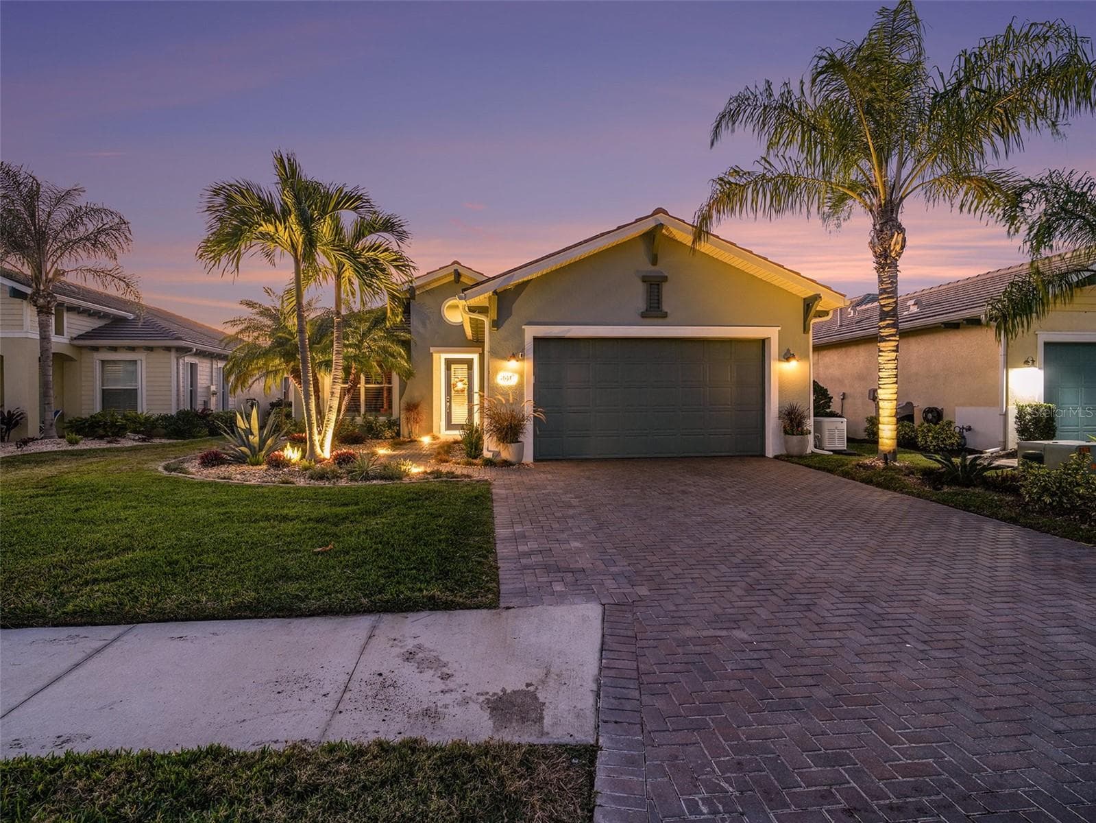 Twilight front exterior with tropical landscaping, paver driveway, and warm lighting that enhances curb appeal. - 1018 OVERLOOK CT, BRADENTON