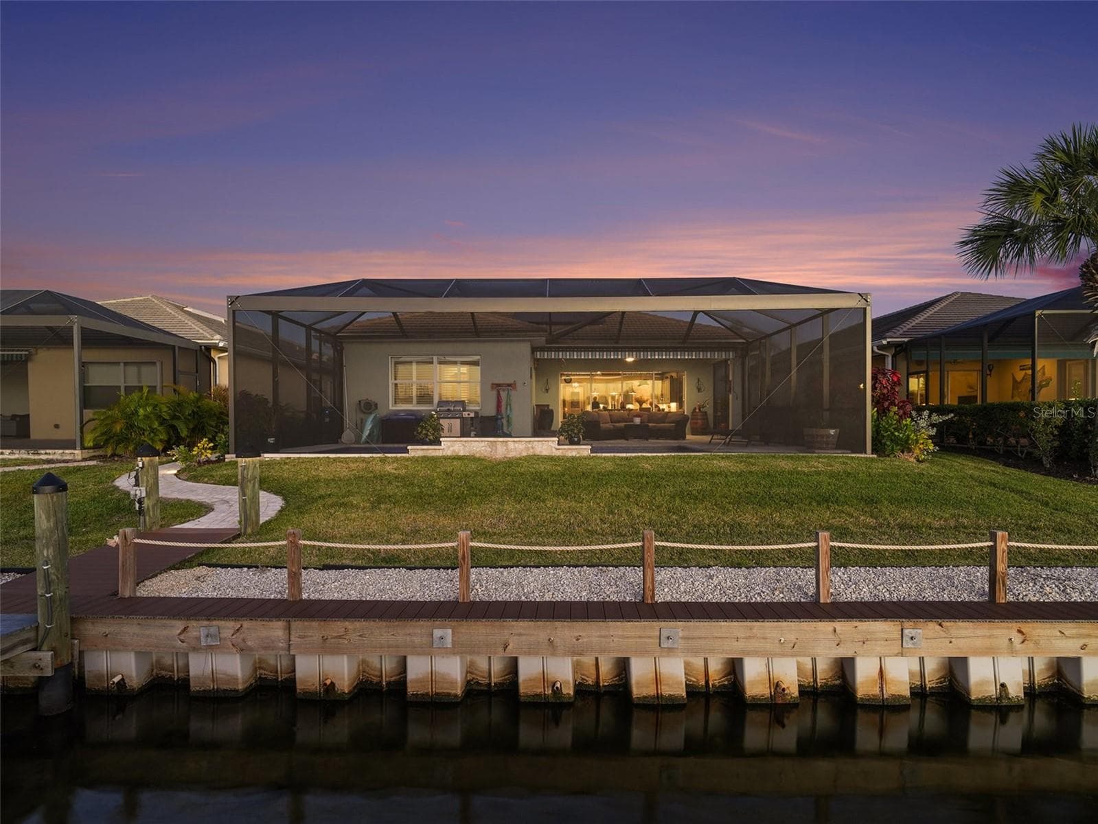 Twilight rear exterior showcasing the home’s waterfront presence, expansive lanai, and resort inspired outdoor ambiance. - 1018 OVERLOOK CT, BRADENTON