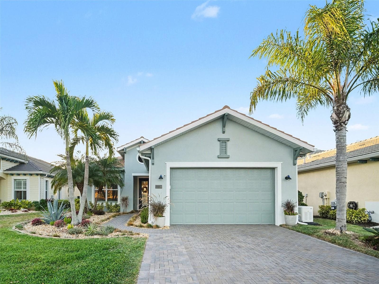 Front exterior with tropical palms, paver driveway, and inviting curb appeal in a beautifully maintained setting. - 1018 OVERLOOK CT, BRADENTON