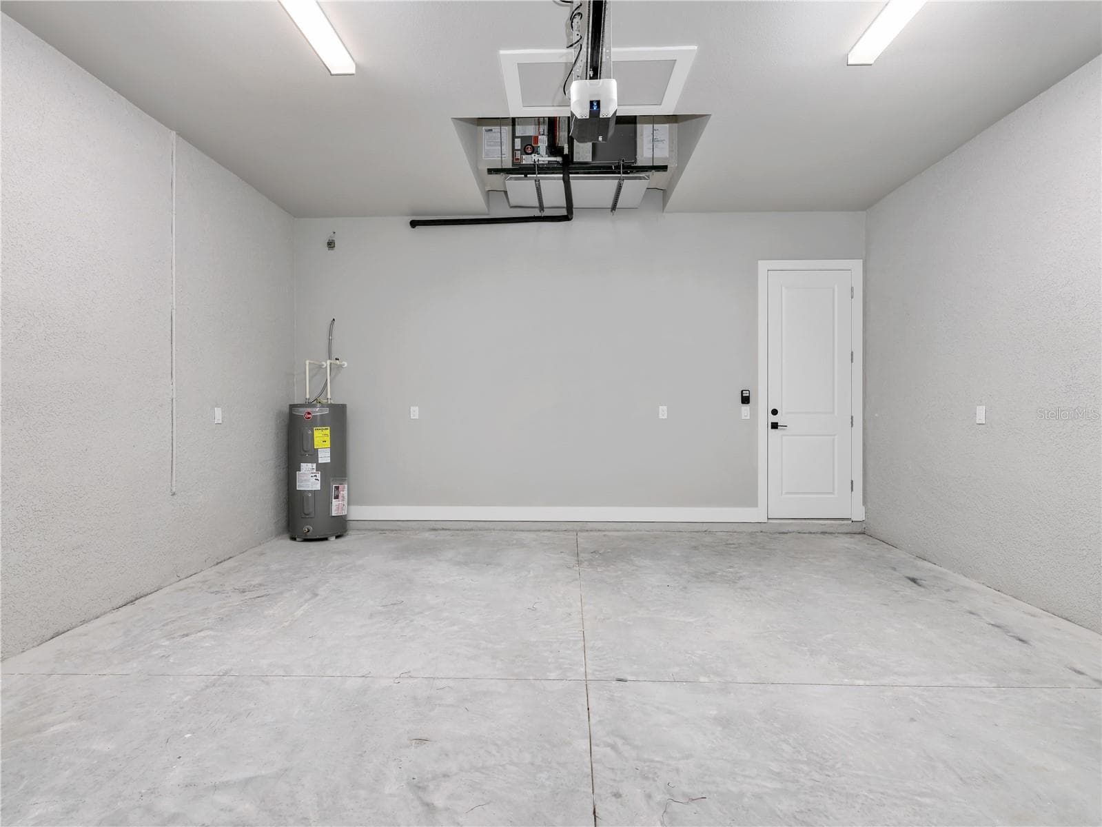 Spacious garage featuring concrete flooring, a water heater, and an overhead garage door opener mechanism - 1310 NW 11TH TER, CAPE CORAL