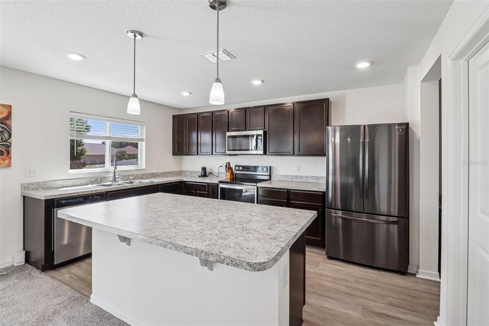The kitchen offers a comfortable, functional design with rich cabinetry, STAINLESS STEEL APPLIANCES, plenty of counter space, and a large ISLAND with bar seating and pendant lighting. - 2082 FICUS ST, MASCOTTE