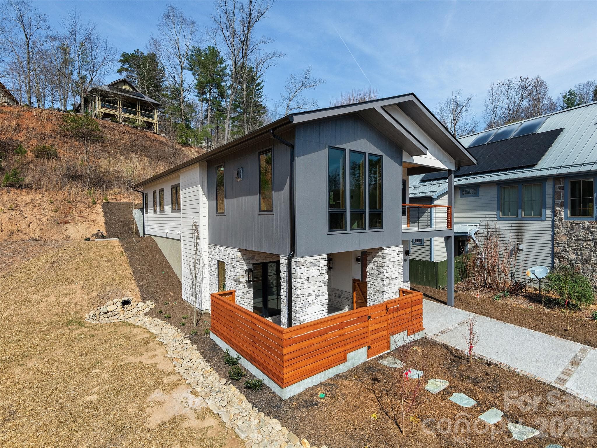 Side/front exterior view of the completed Courtyard Villa highlighting contemporary design, cement HardiePlank siding, cultured stone accents, private courtyard entry, covered porch, and low-maintenance landscaping. - Asheville