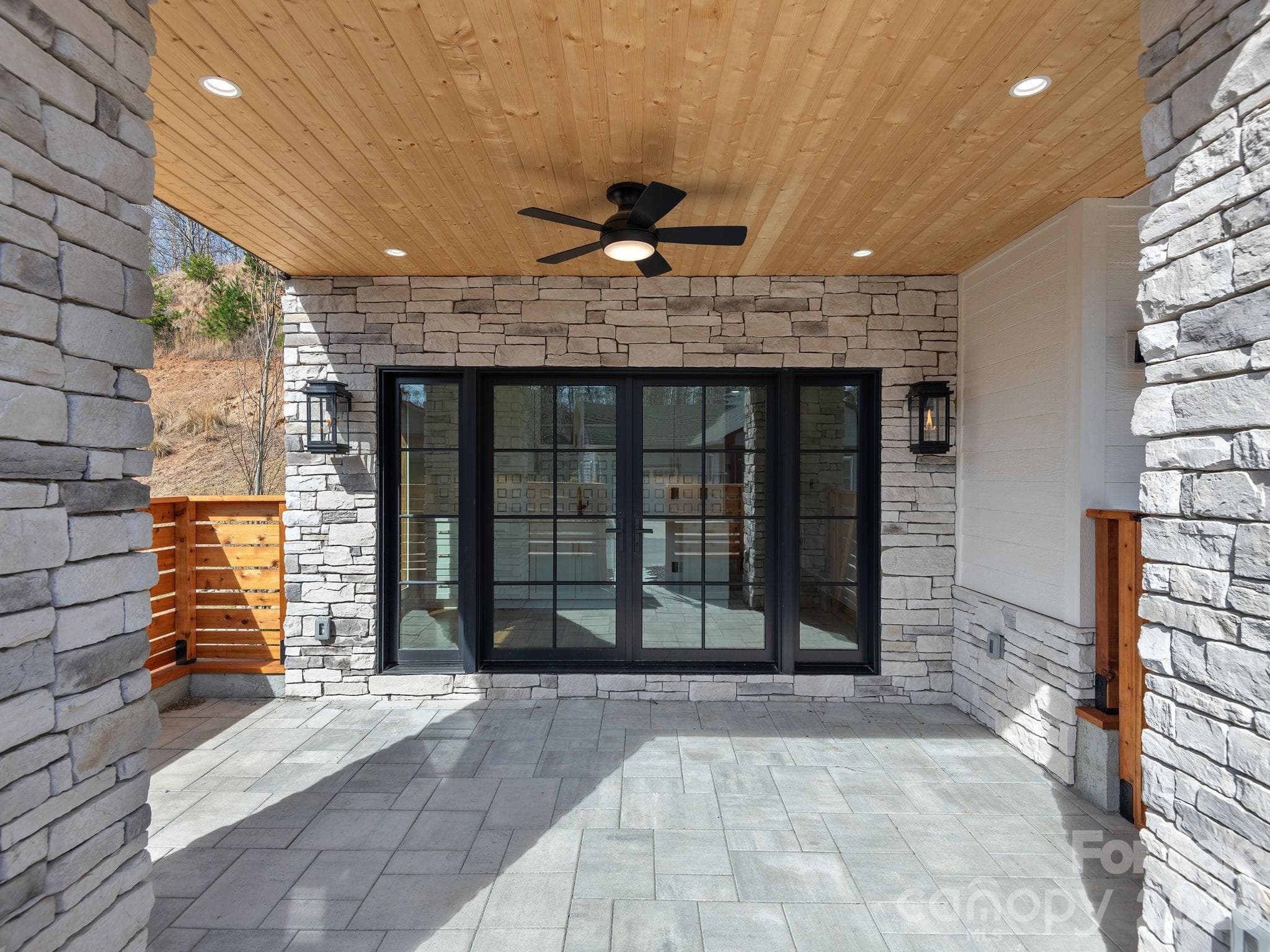 Representative photo from 50 Verde Drive showing the builder’s quality of construction and finish level, including the covered entry, cultured stone, tongue-and-groove wood ceiling, natural gas lanterns, and concrete patio. - Asheville
