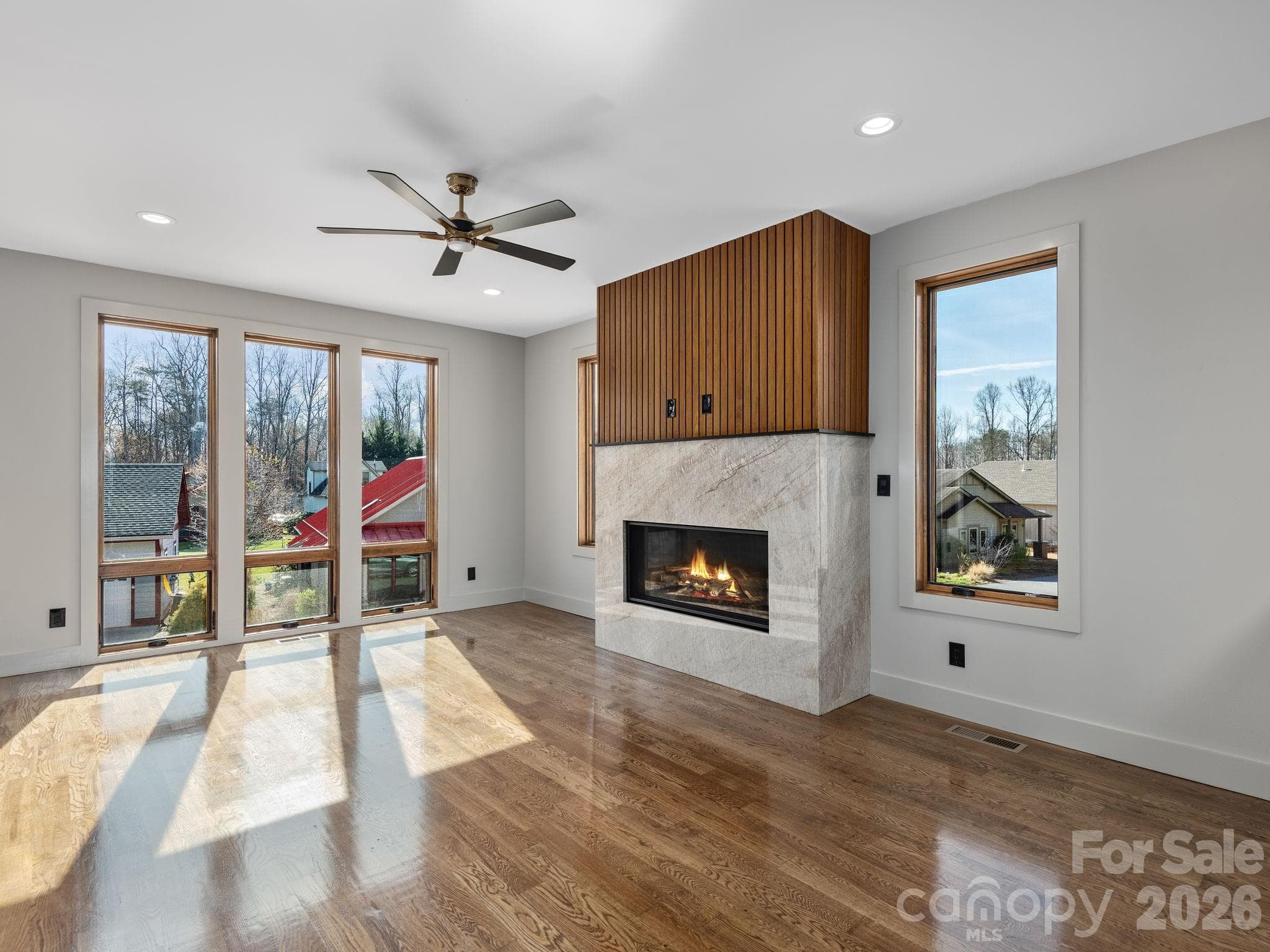 Representative photo from 50 Verde Drive showing the builder’s quality of construction and finish level, including oak hardwood floors, expansive windows, and a vented gas fireplace with granite surround and custom wood accent detail. - Asheville