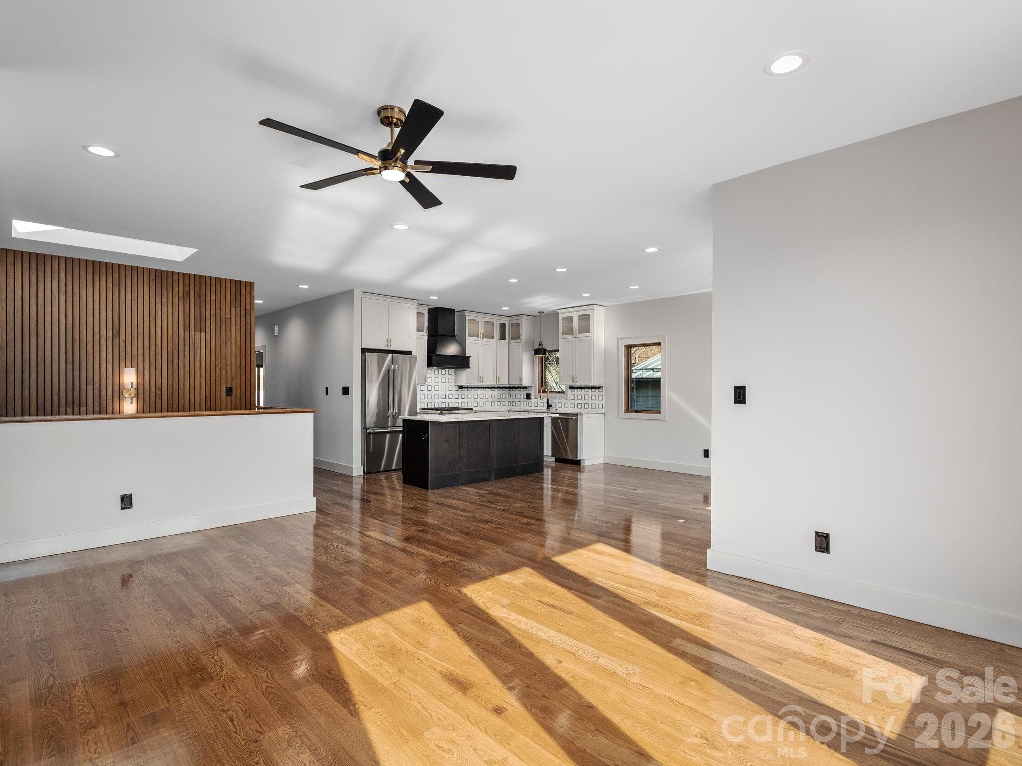 Representative photo from 50 Verde Drive showing the builder’s quality of construction and finish level, including the open-concept main living area with oak hardwood floors and seamless flow to the kitchen, hall, stairwell, and elevator access. - Asheville