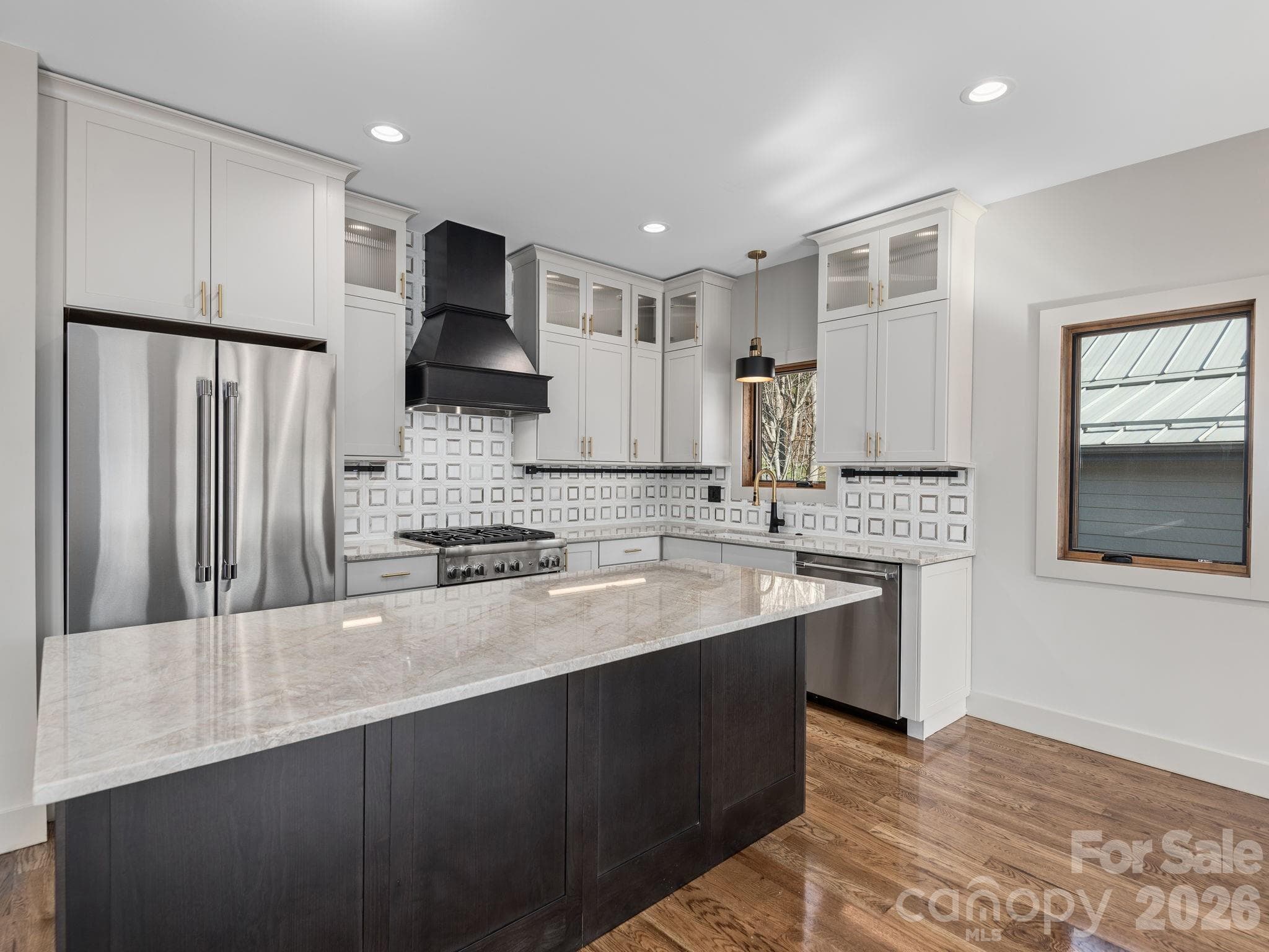 Representative photo from 50 Verde Drive showing the builder’s quality of construction and finish level, including granite countertops, large center island, Thermador appliances, Wolf Home Products cabinetry, and striking tile backsplash. - Asheville