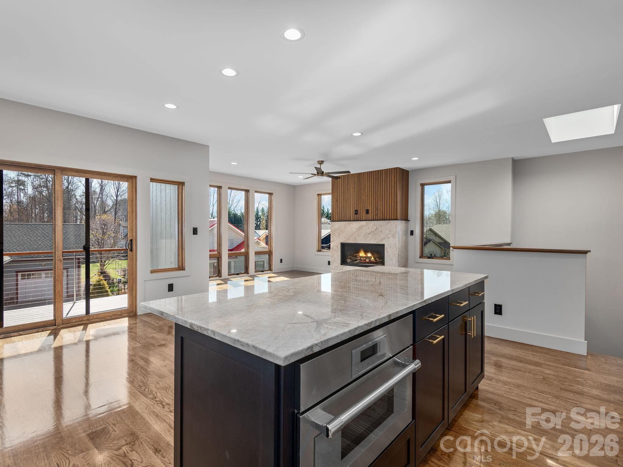 Representative photo from 50 Verde Drive showing the builder’s quality of construction and finish level, including the oversized kitchen island, oak hardwood floors, vented gas fireplace, and sliding doors opening to the covered deck. - Asheville