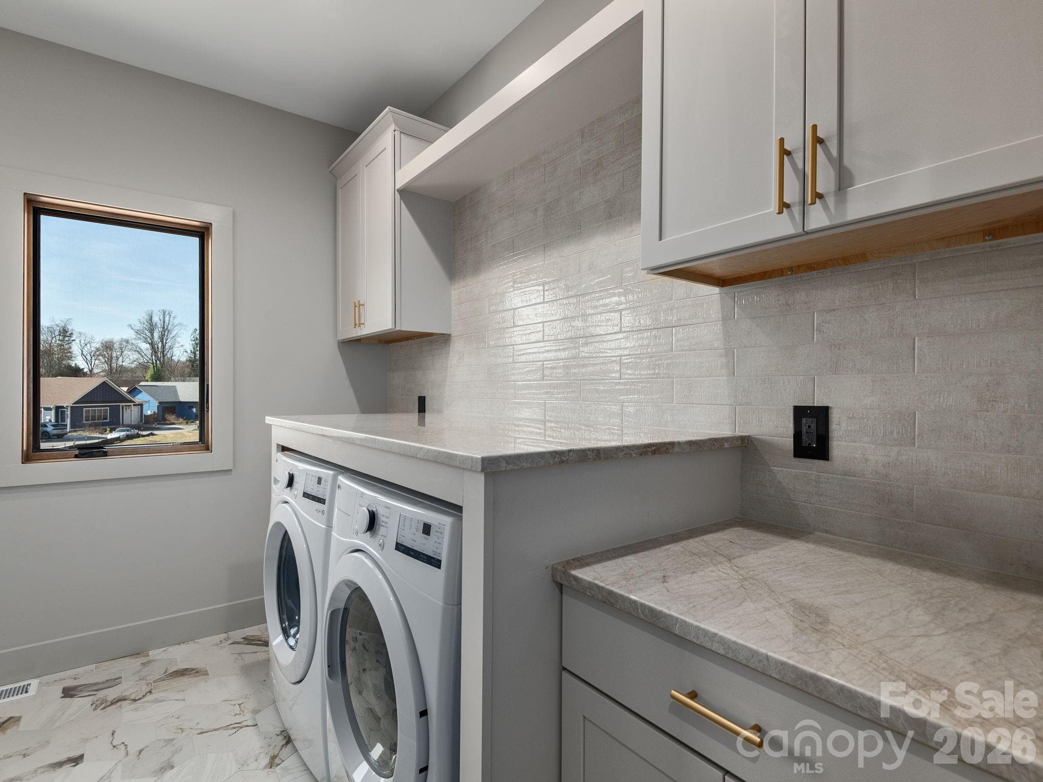 Representative photo from 50 Verde Drive showing the builder’s quality of construction and finish level, including the laundry room with GE front-load washer and electric dryer, granite countertops, large tiled backsplash, ceramic tile floors, and Wolf cabinetry. - Asheville