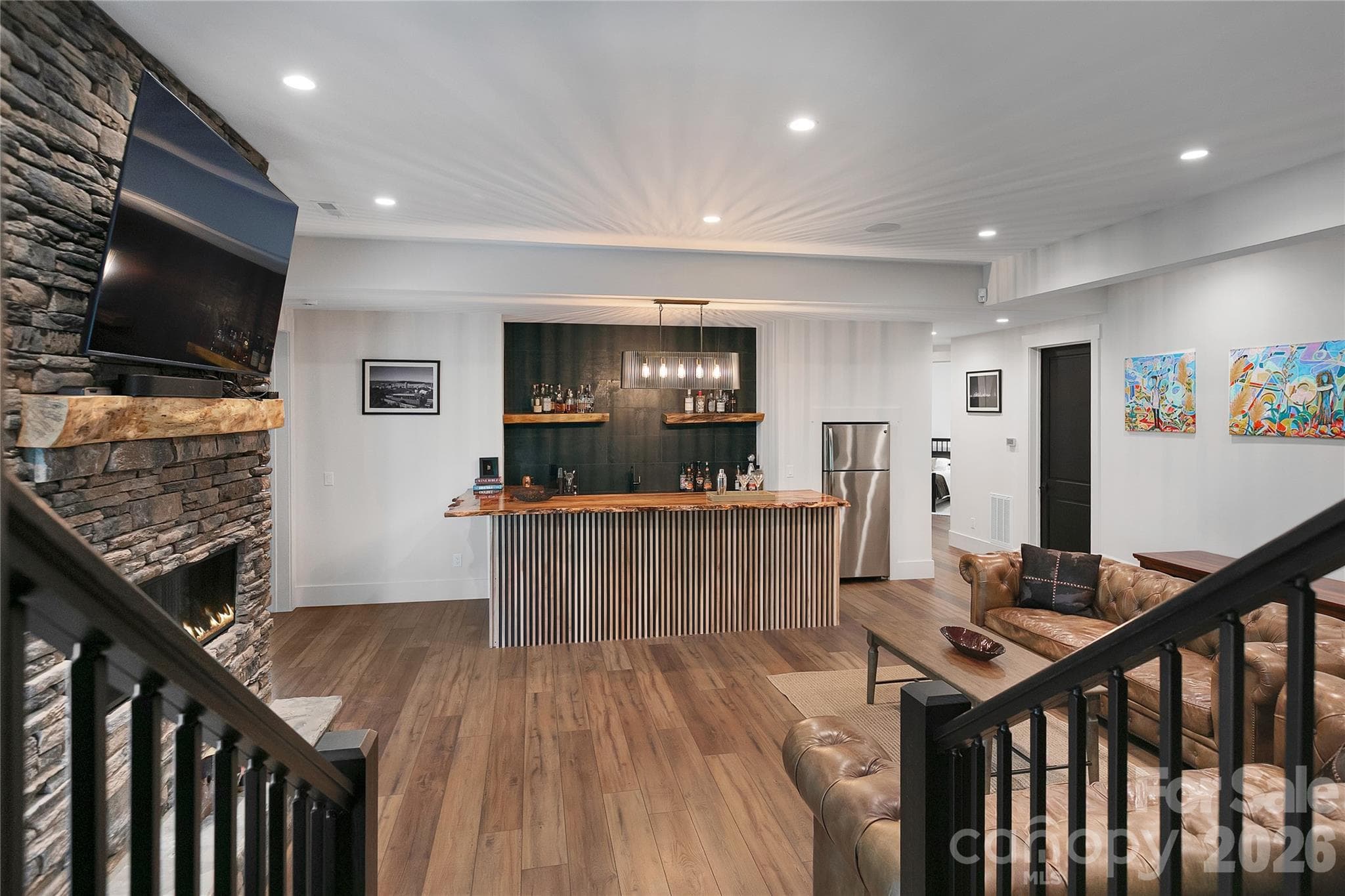 Designed for entertaining, the lower level family room offers the perfect gathering space with a striking stone fireplace and a handcrafted wood bar topped with a live edge countertop. - Brevard